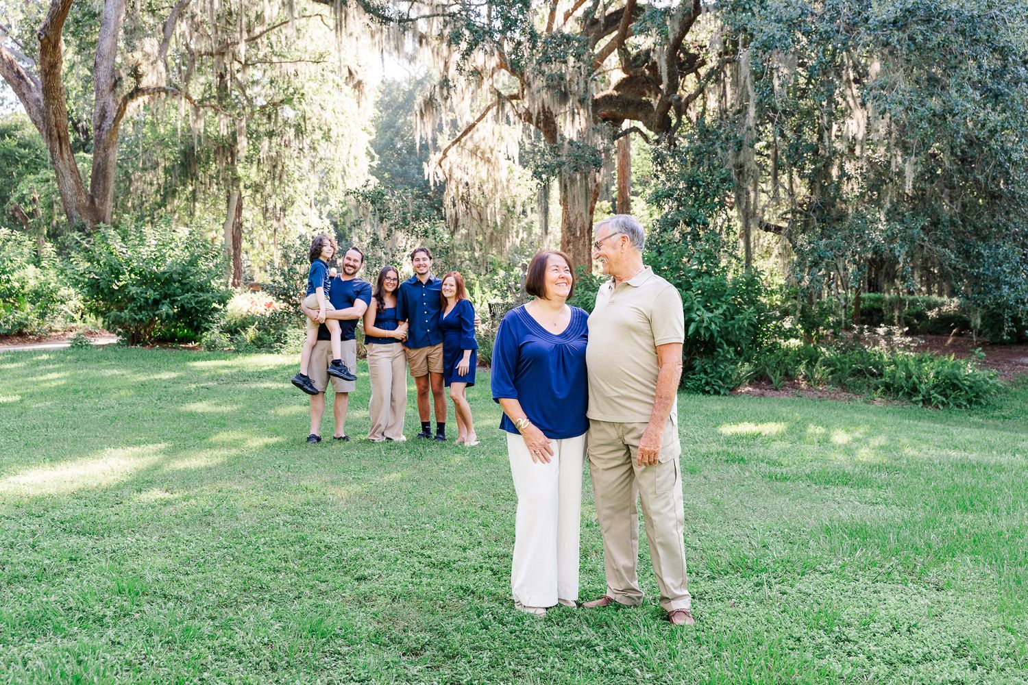 Farm-style outdoor wedding ceremony guests walking along a path in a lush green garden setting under sunlit trees.