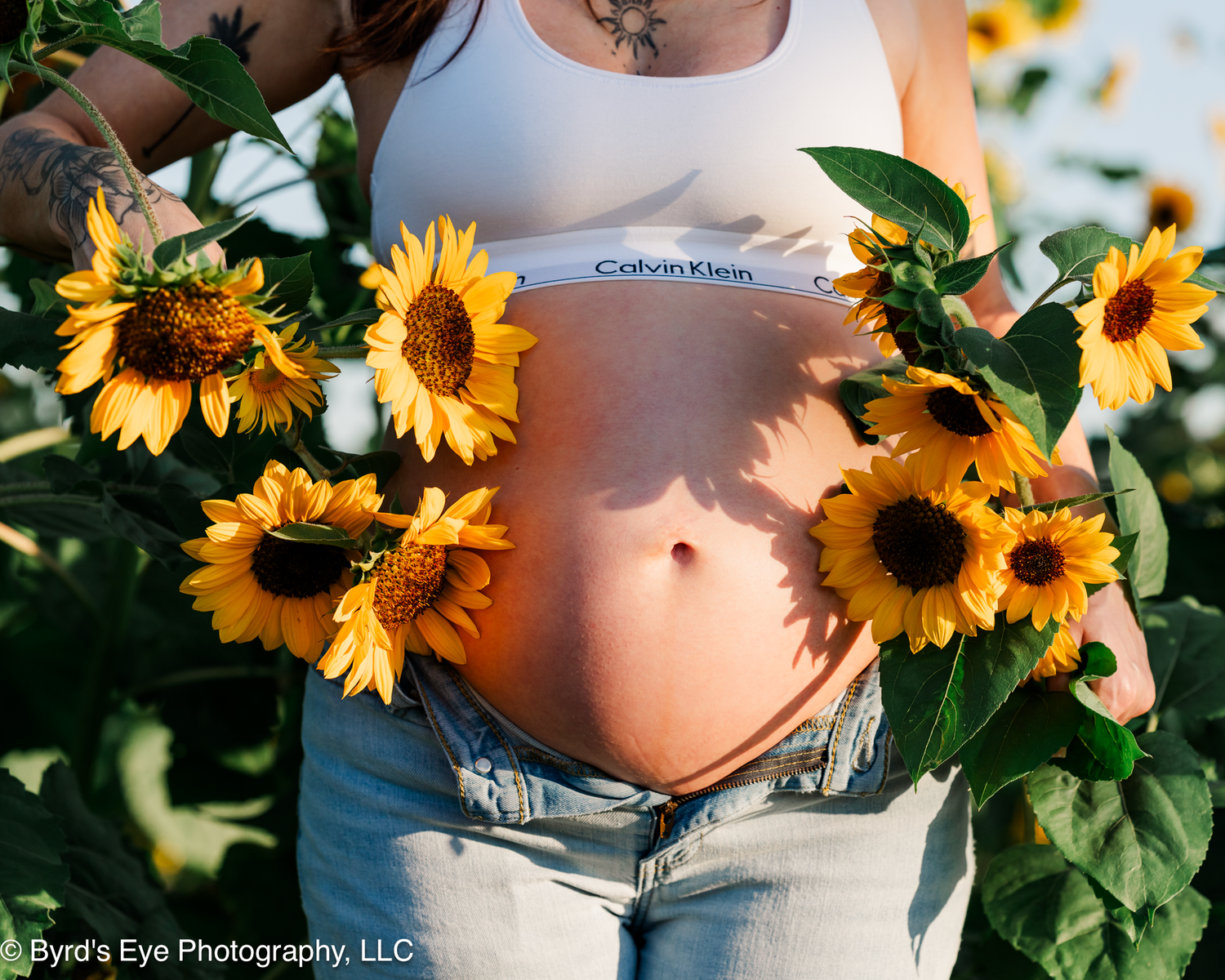 Artistic maternity photography with vibrant sunflowers against a sunny outdoor backdrop.