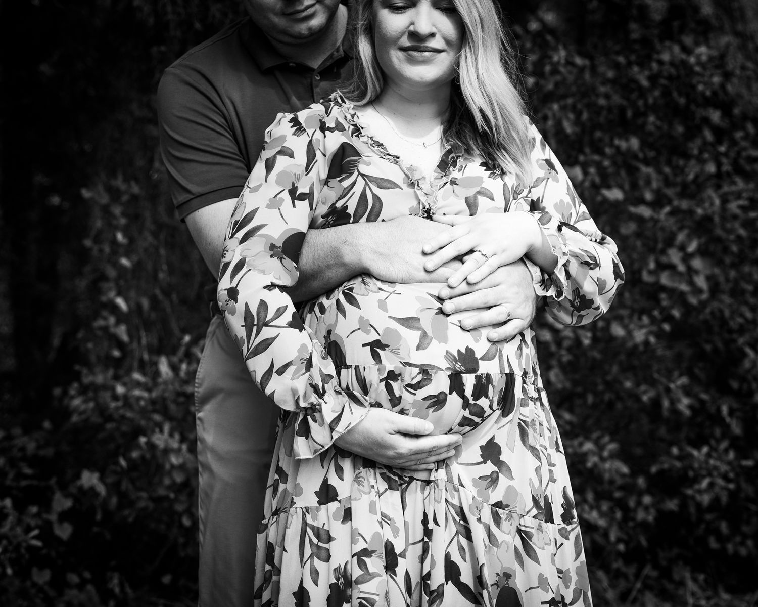 A couple wearing matching white and floral attire pose together on the lawn in black and white photography.