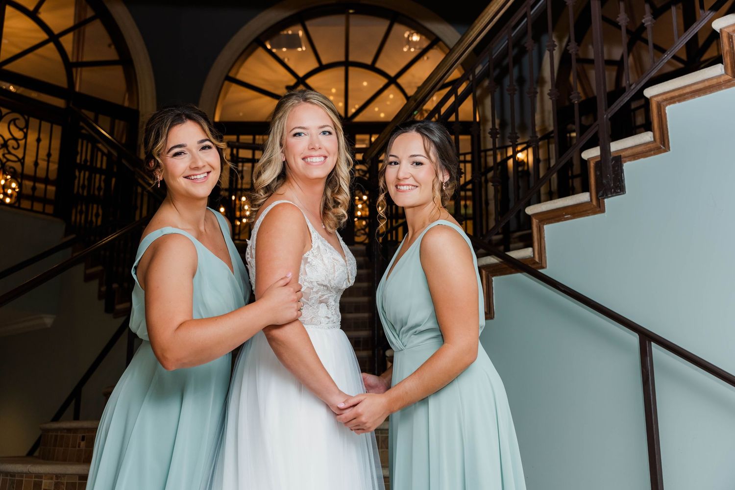 Bridesmaids in seafoam green dresses pose on elegant staircase.