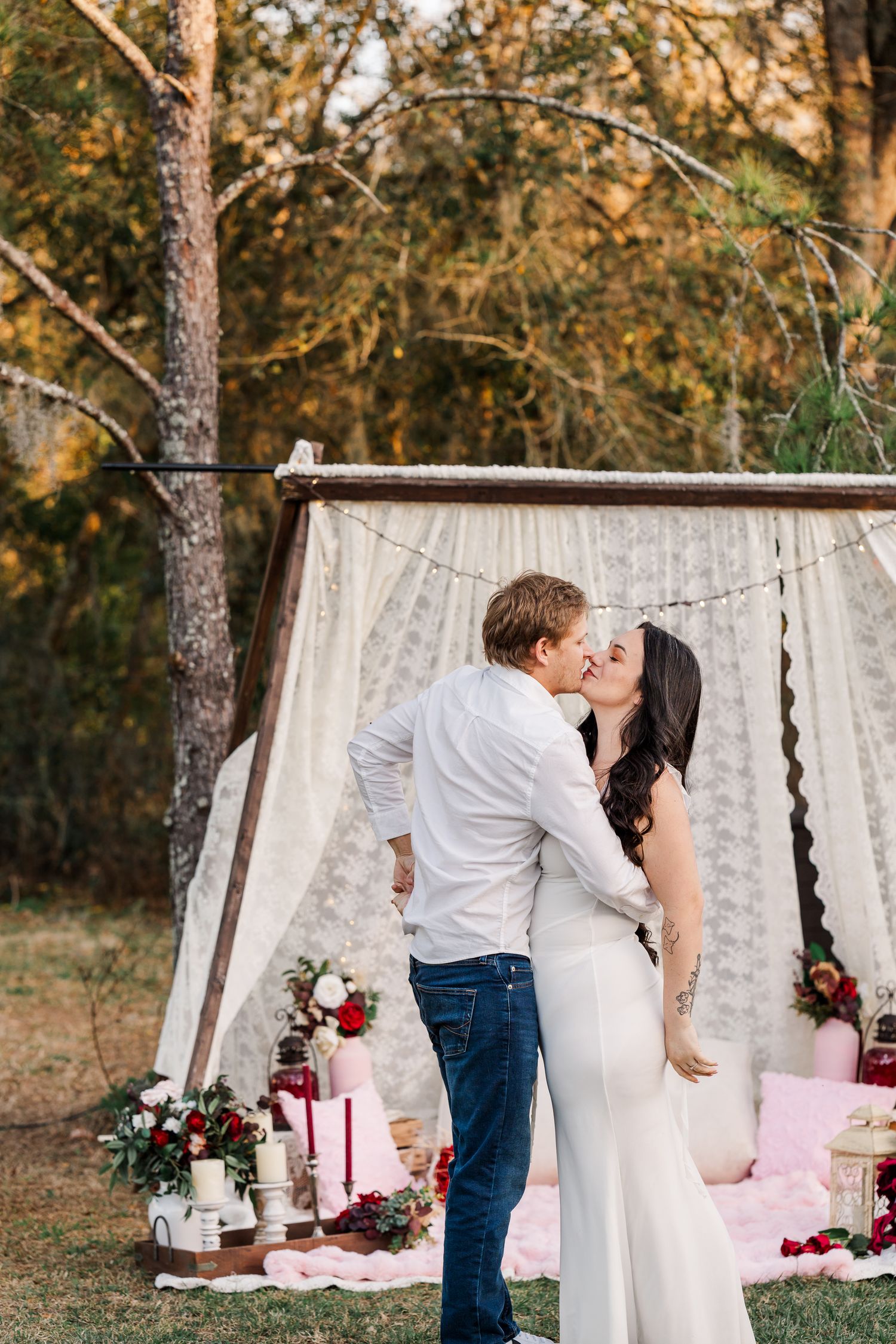 A romantic outdoor scene with a white backdrop and pink decor elements arranged in a wooded setting at sunset.