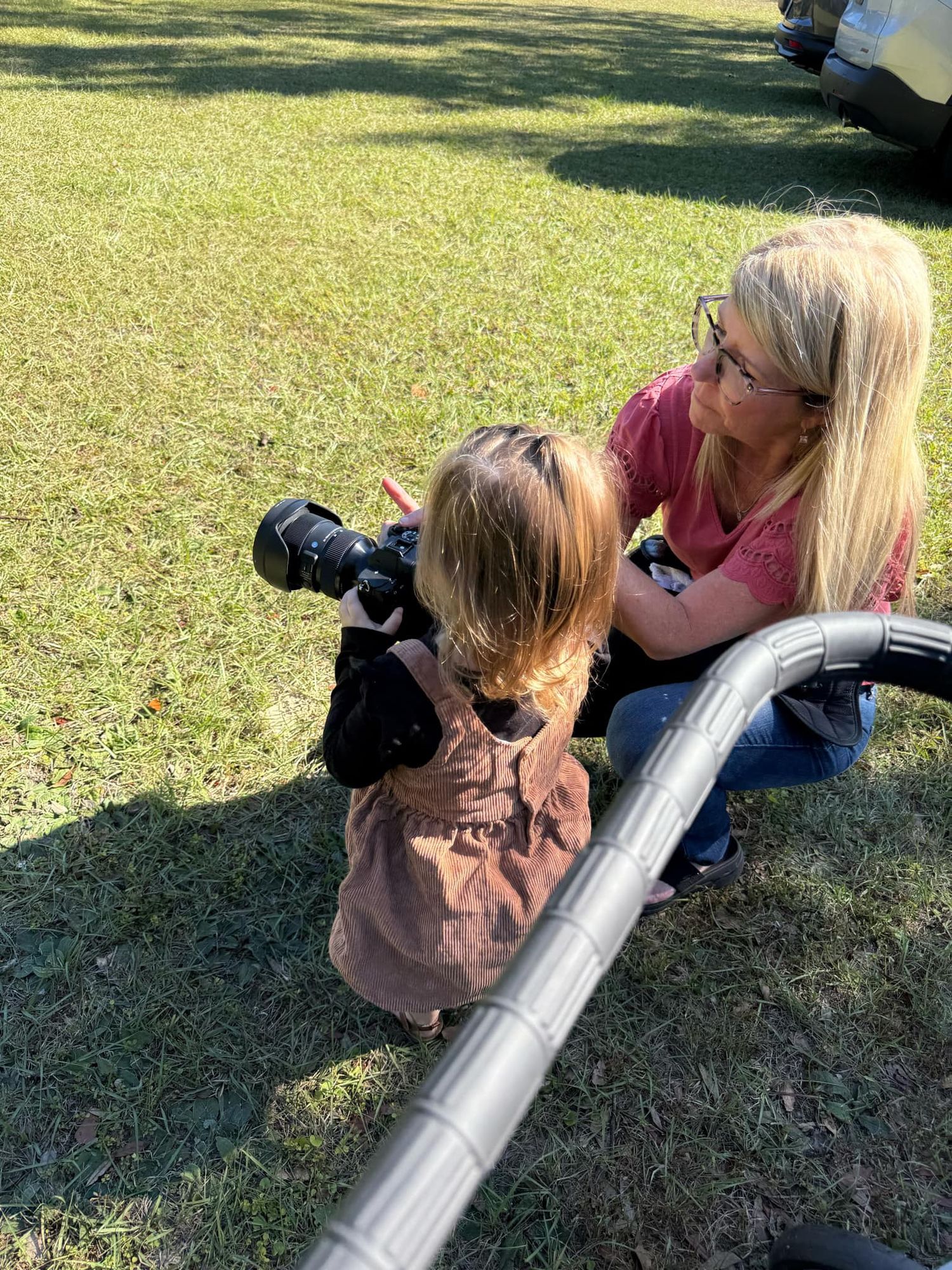Photographer using a telephoto lens to take close-up shots on a sunny day. Teaching a child how to use the camera during their session.