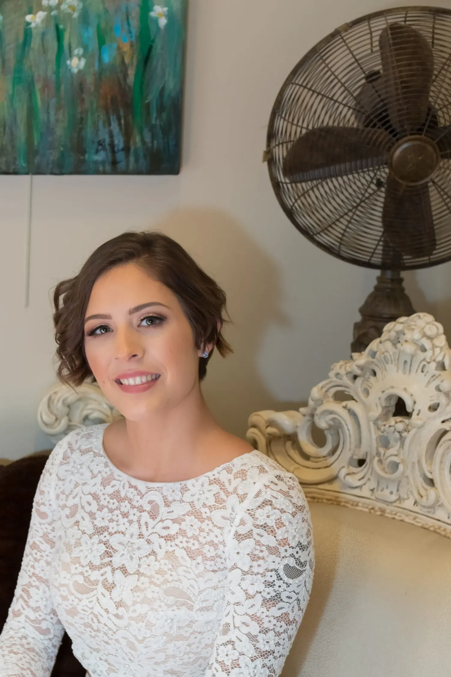 A woman wears a white lace wedding dress while sitting on an ornate white vintage chair, shown in a series of poses.