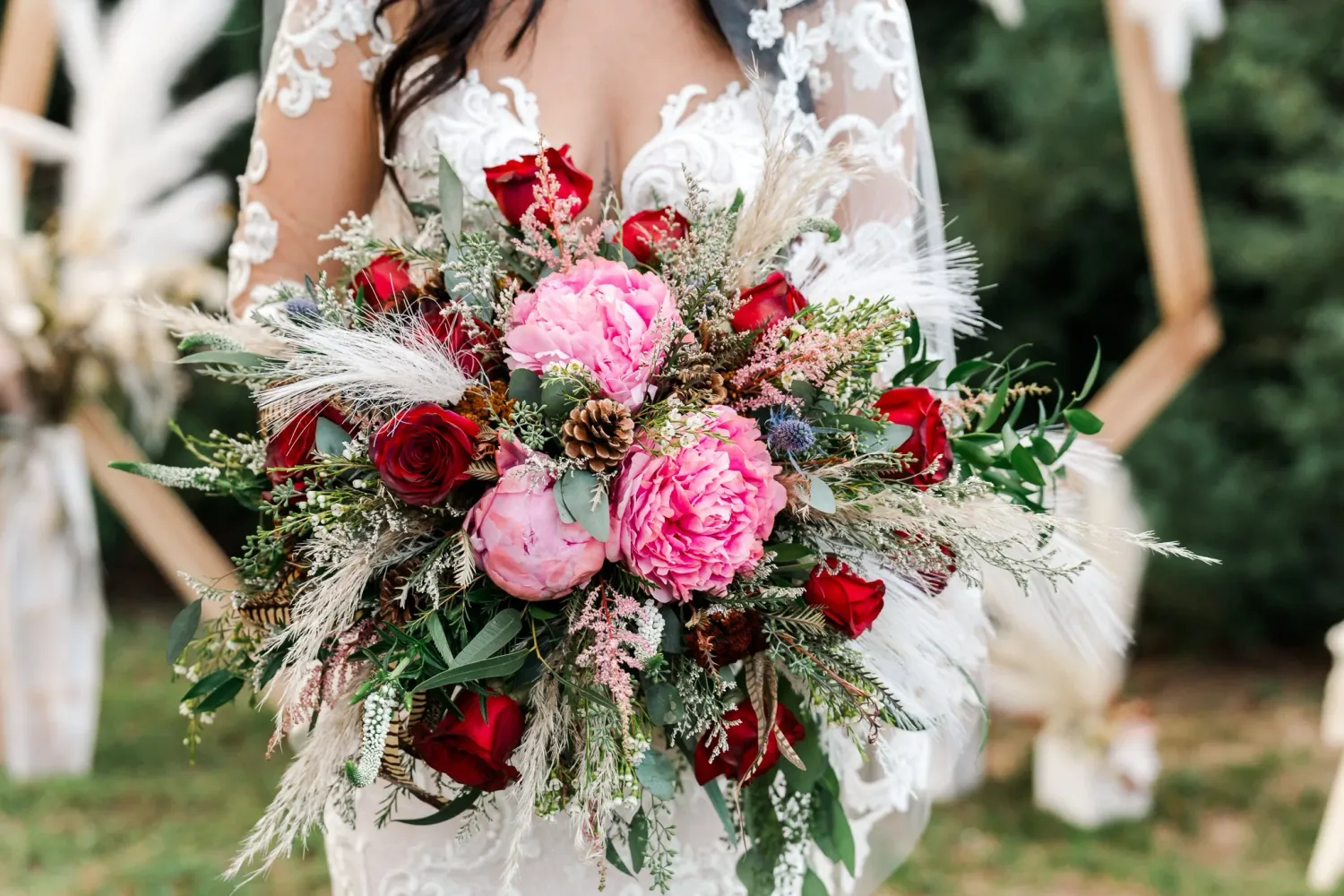Elegant bridal bouquet with lush pink and red roses, delicate greenery, and white accents captured in natural outdoor setting.