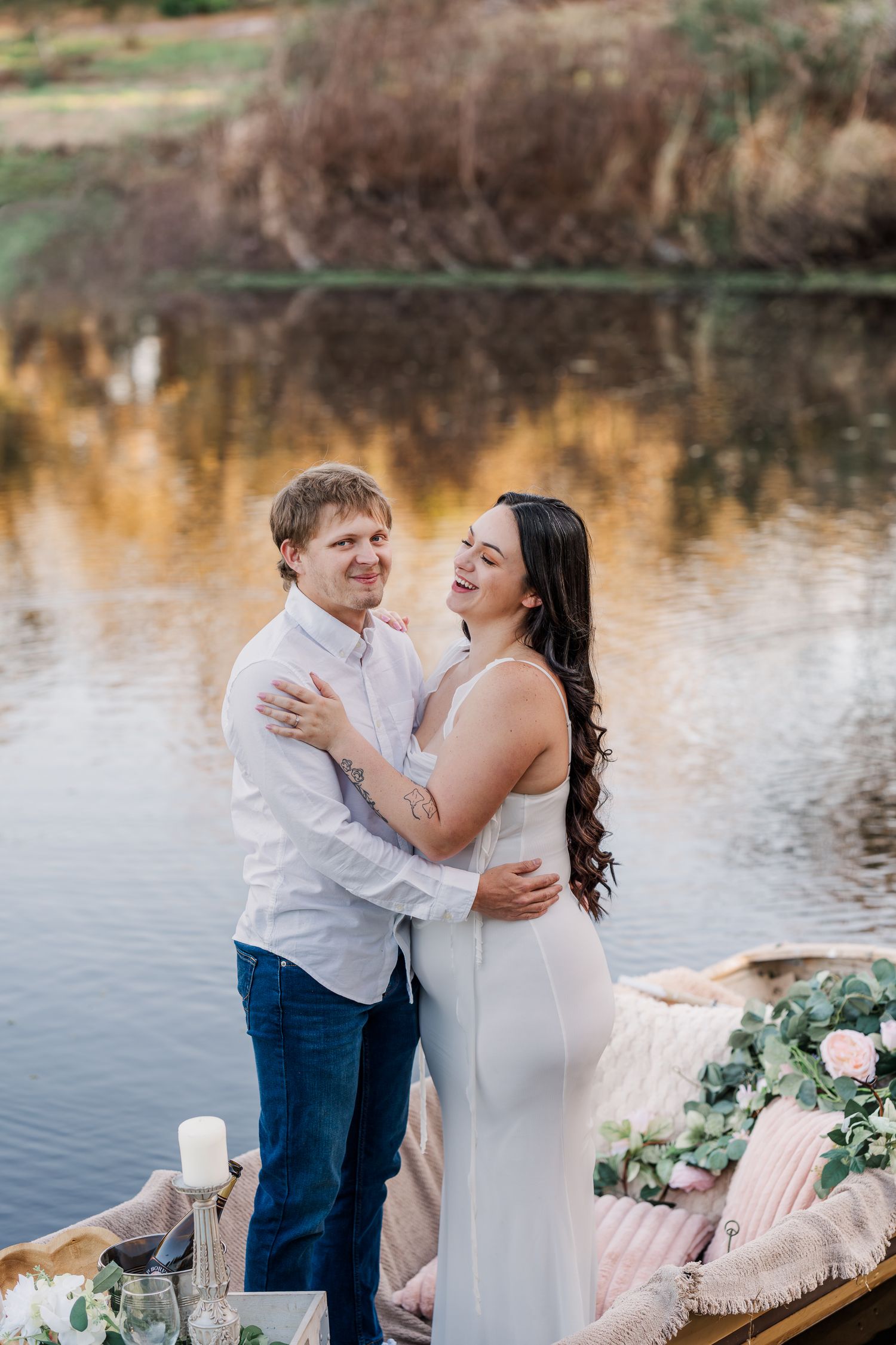 Tender moment shared between parent and child by a serene lake with floral decorations and soft lighting at sunset.