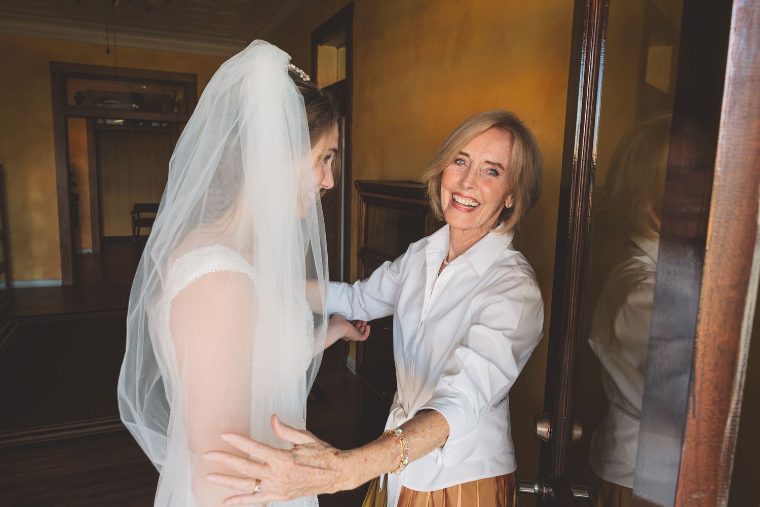 A heartwarming moment between a bride in her wedding gown and veil and a woman in a white blazer sharing joyful laughter.