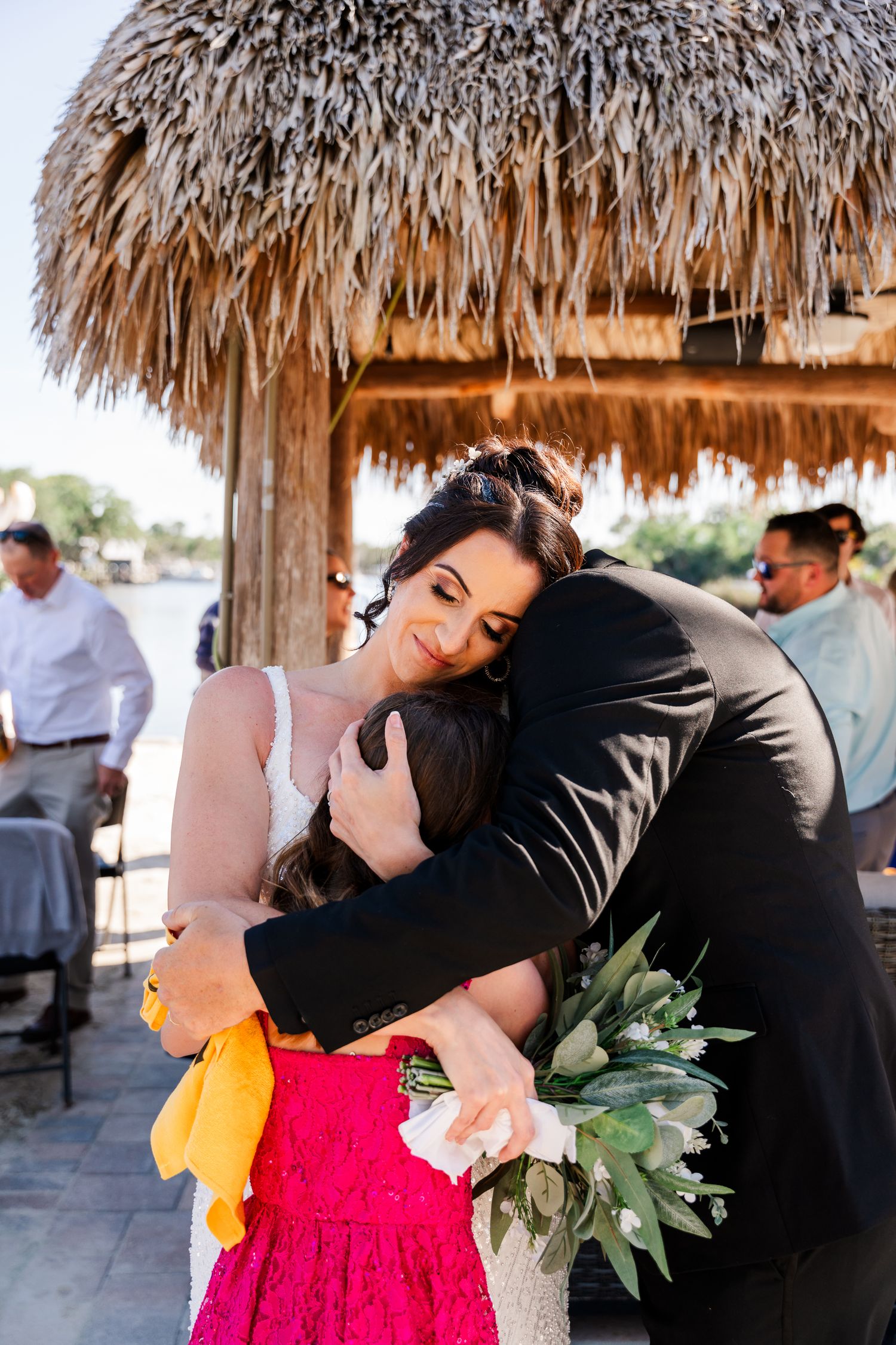 A heartfelt embrace between two people under a thatched tiki hut during a tropical beach gathering.