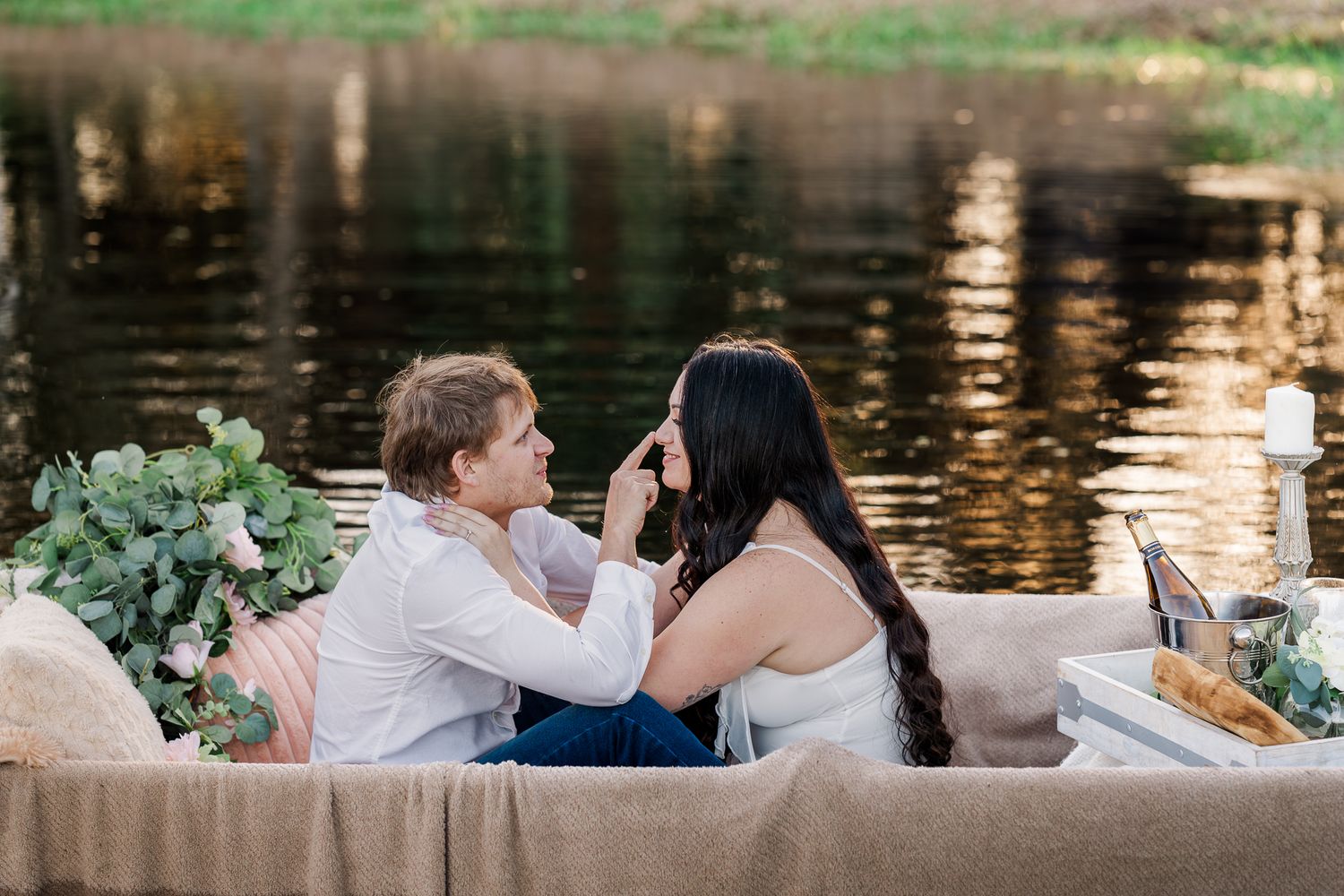 Romantic couple sharing a tender moment by a serene lake during sunset with reflections on the water.