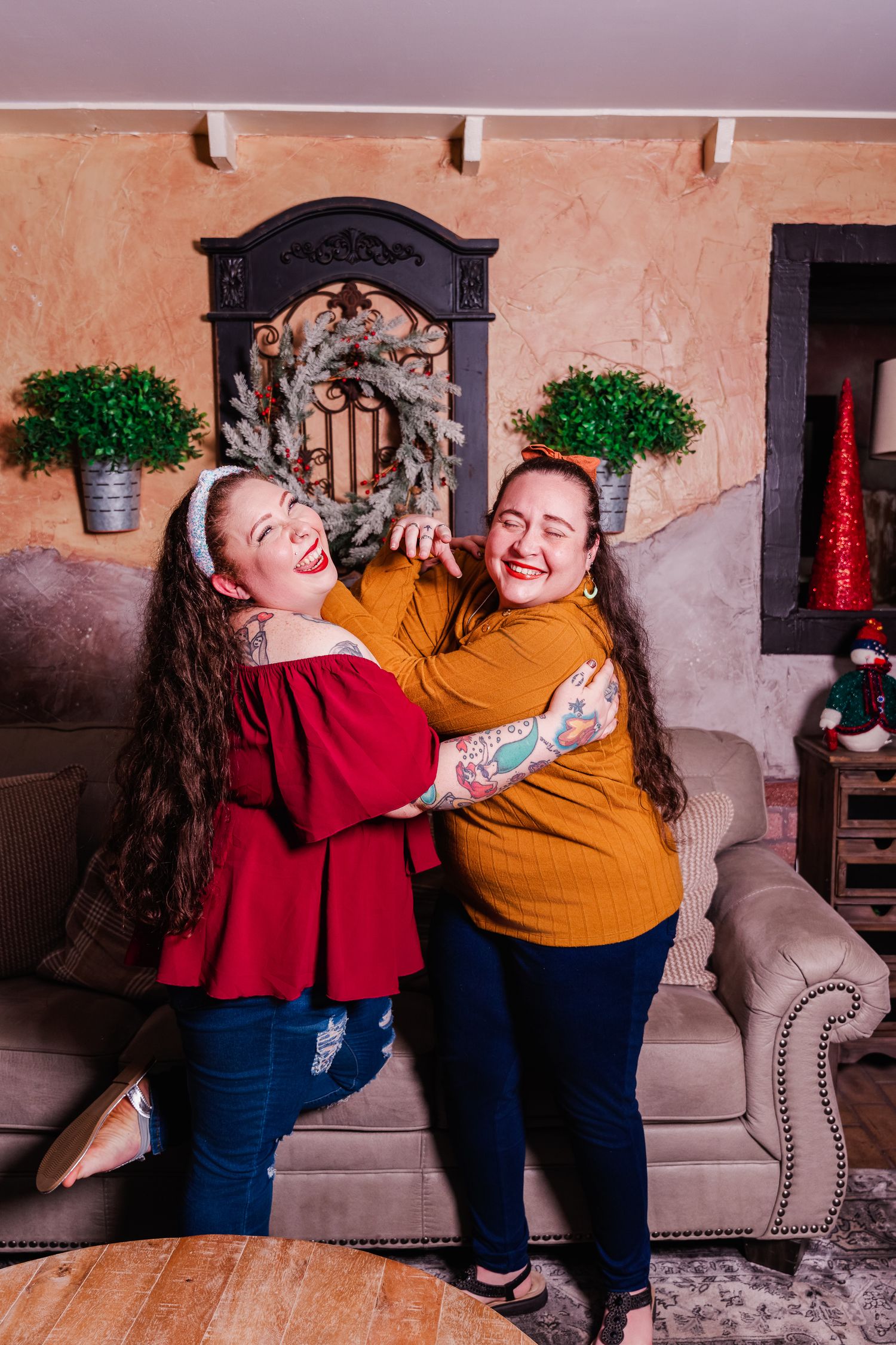 Two people in festive sweaters sharing joyful moment on couch with holiday decor.