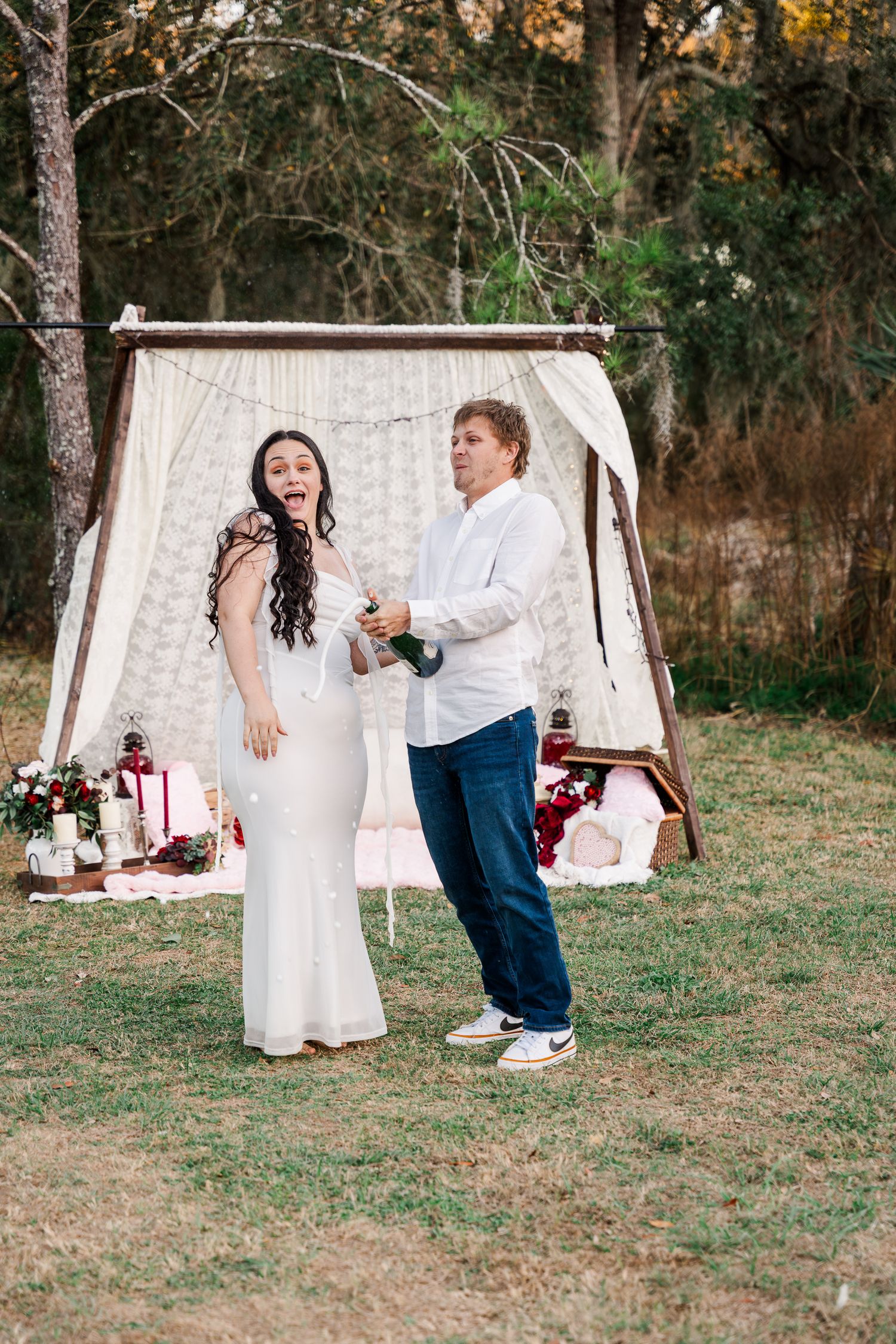 A couple dances playfully in front of a white tent backdrop during an outdoor event on grassy terrain.