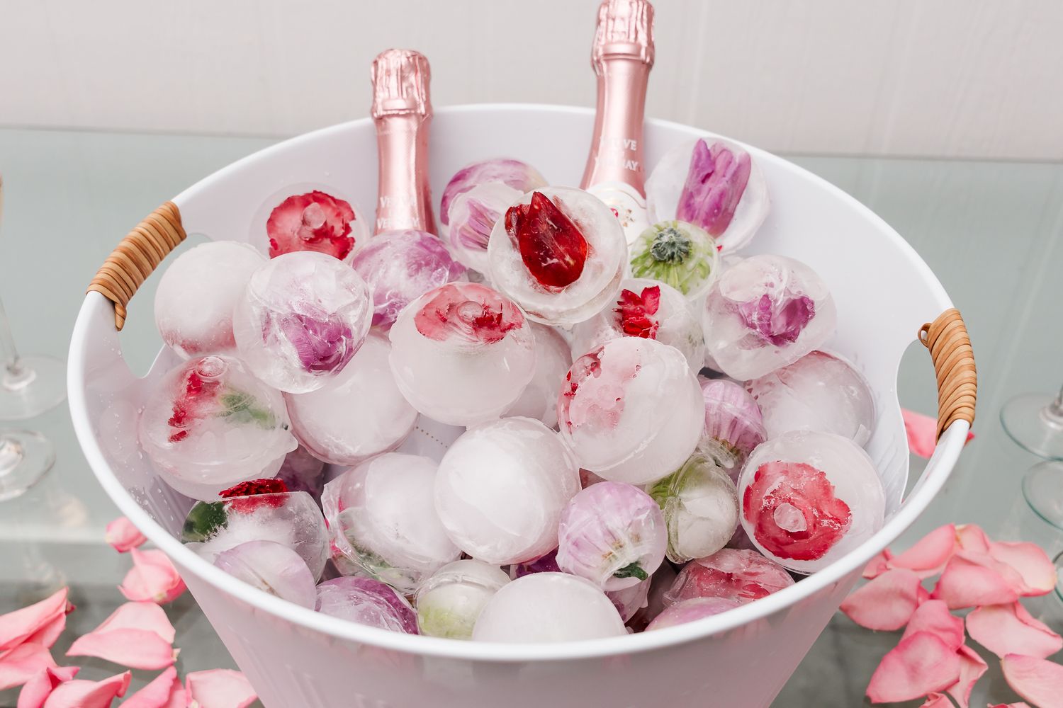Pink champagne bottles chill in an ice bucket with frozen rose petals and flower buds for elegant entertaining.
