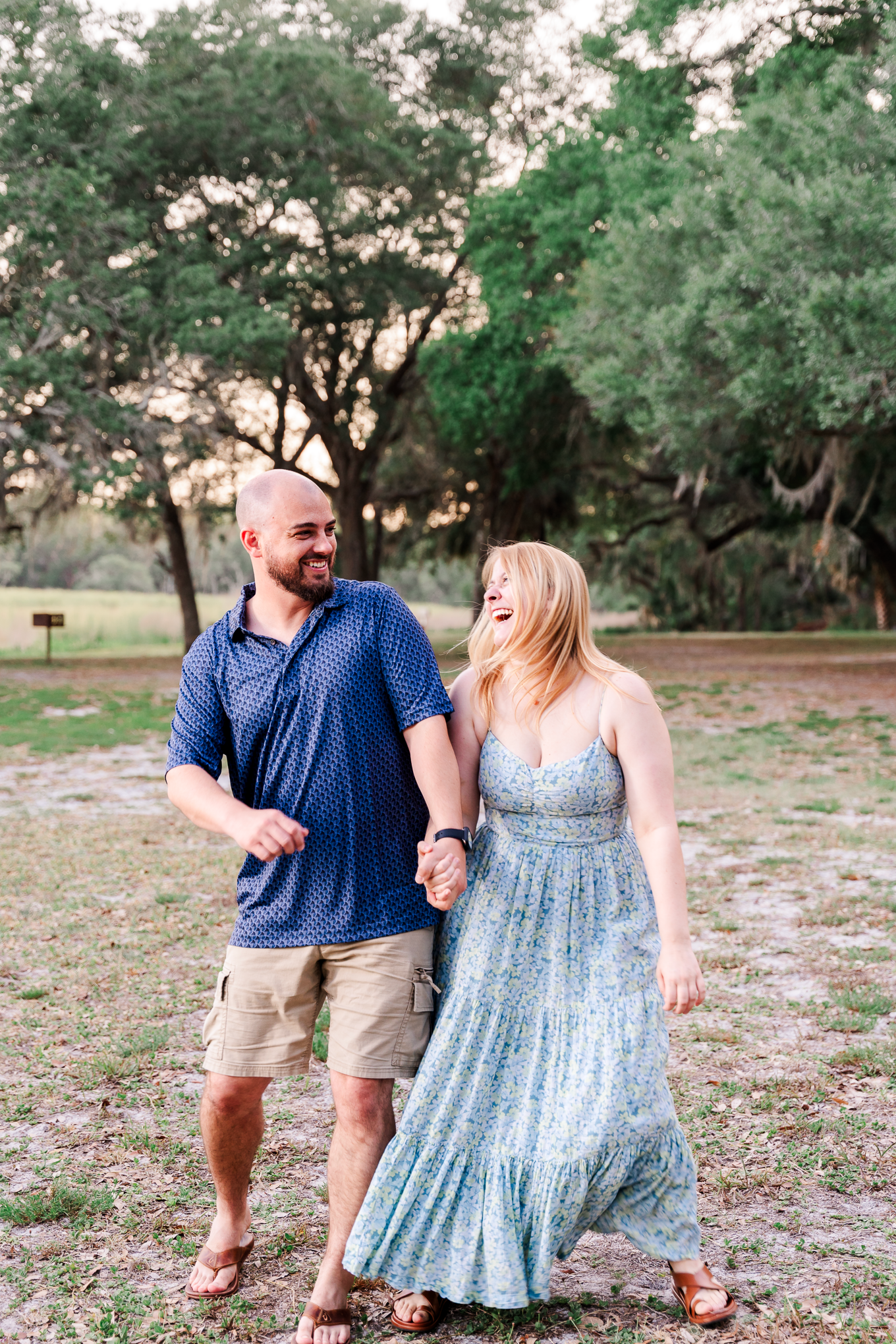 Couple walking and laughing together in a park at sunset.