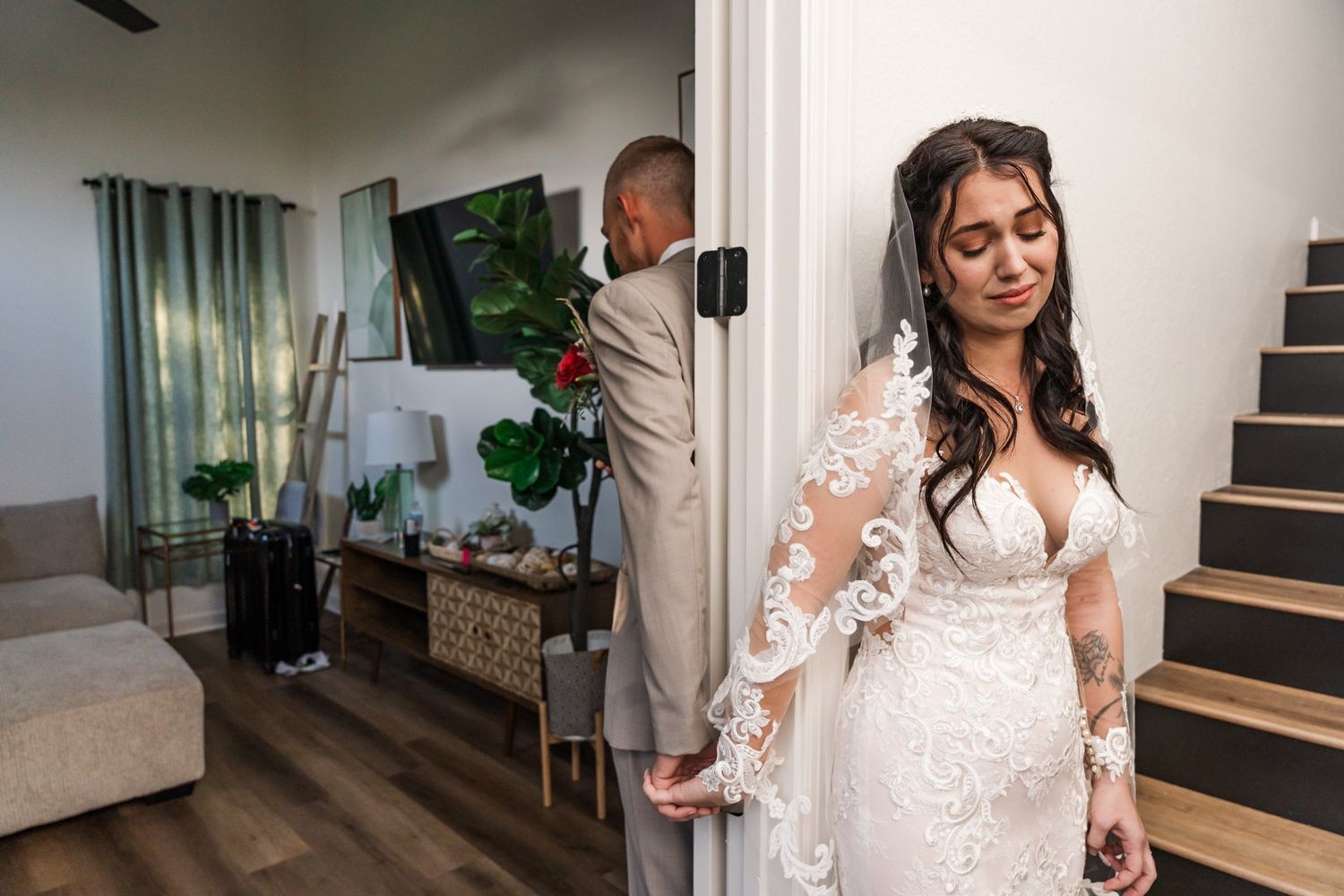 First look wedding moment with couple separated by doorway in modern home interior with hardwood floors and stairs.