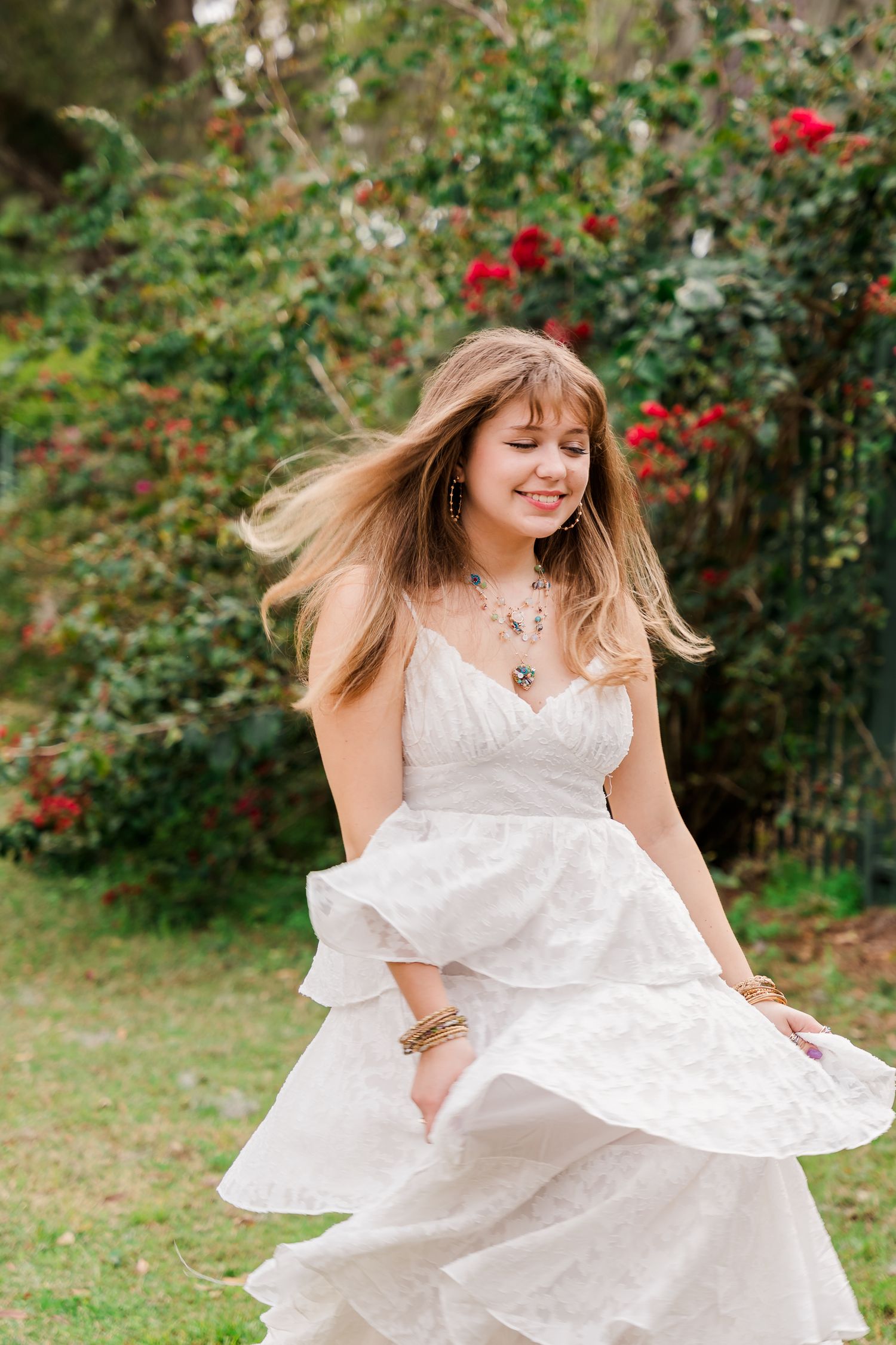Joyful spinning portrait in white dress surrounded by blooming garden flowers.