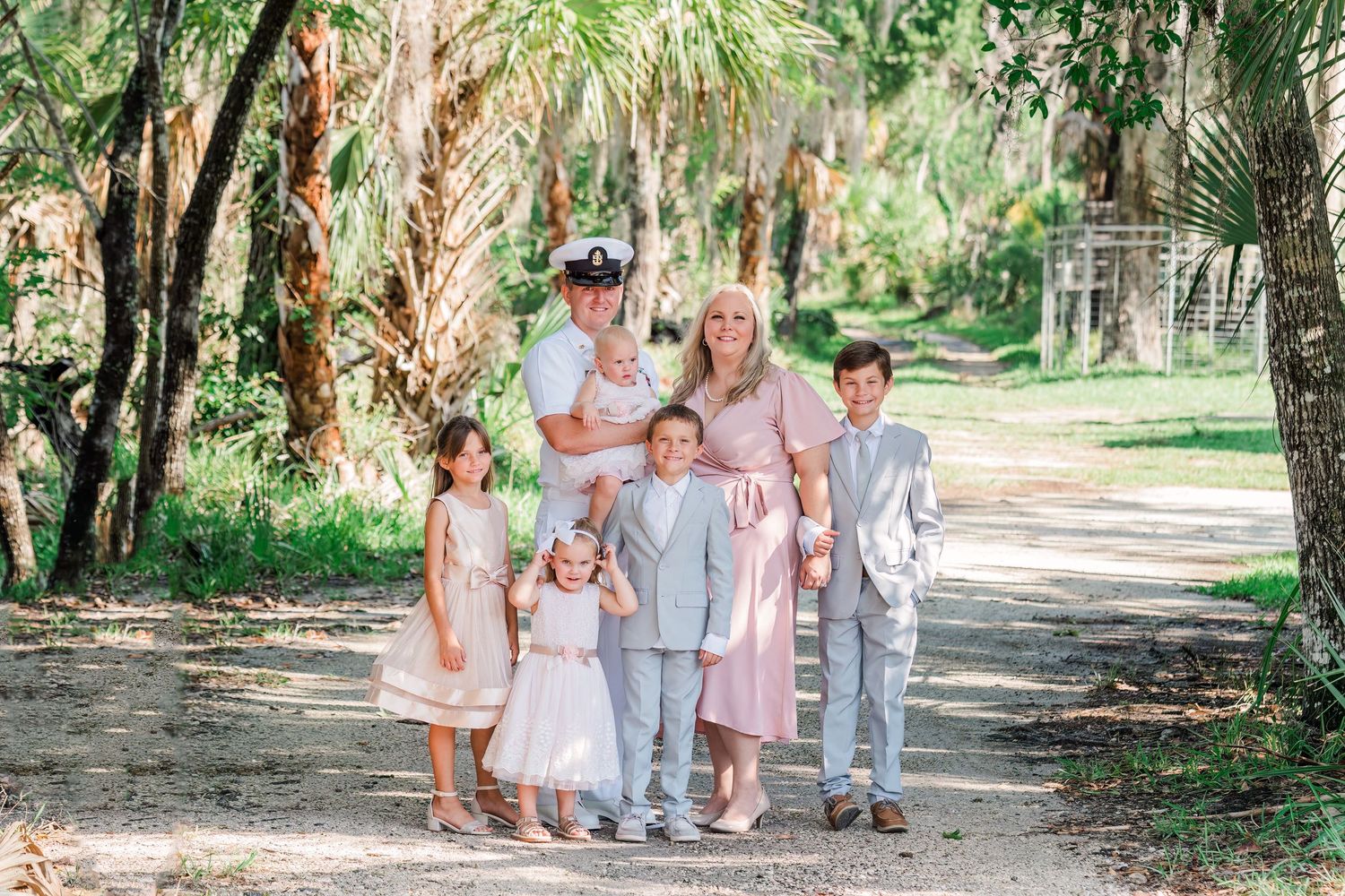 A group stands together on a sandy path surrounded by palm trees and lush tropical foliage in matching pastel outfits.