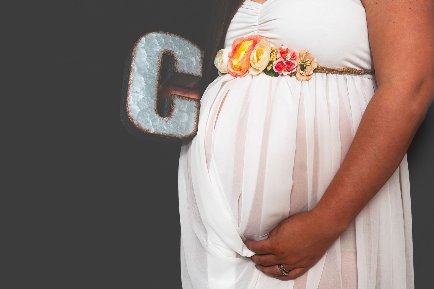 A white maternity dress shown from different angles highlights a growing baby bump, floral embellishments and flowing fabric.