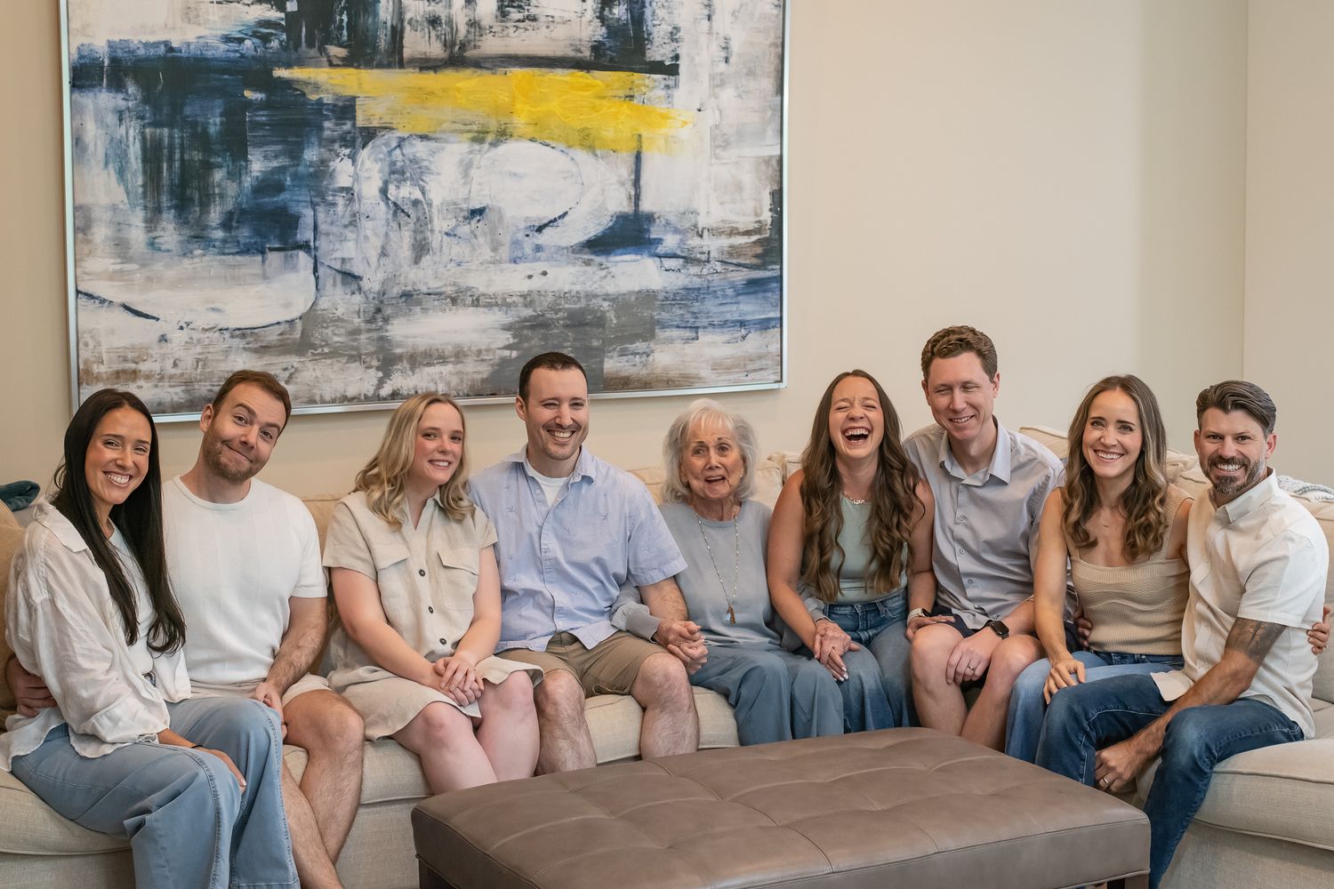 Large family group smiling together on a couch in a modern living room with abstract art on the wall.