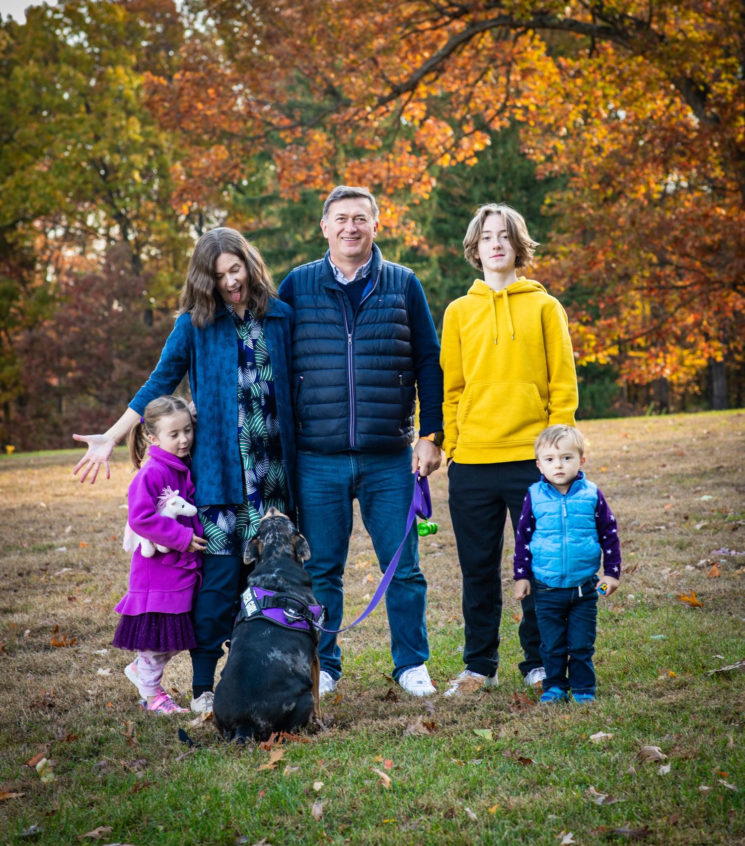 A group enjoys a fall photoshoot outdoors with colorful autumn foliage in the background.