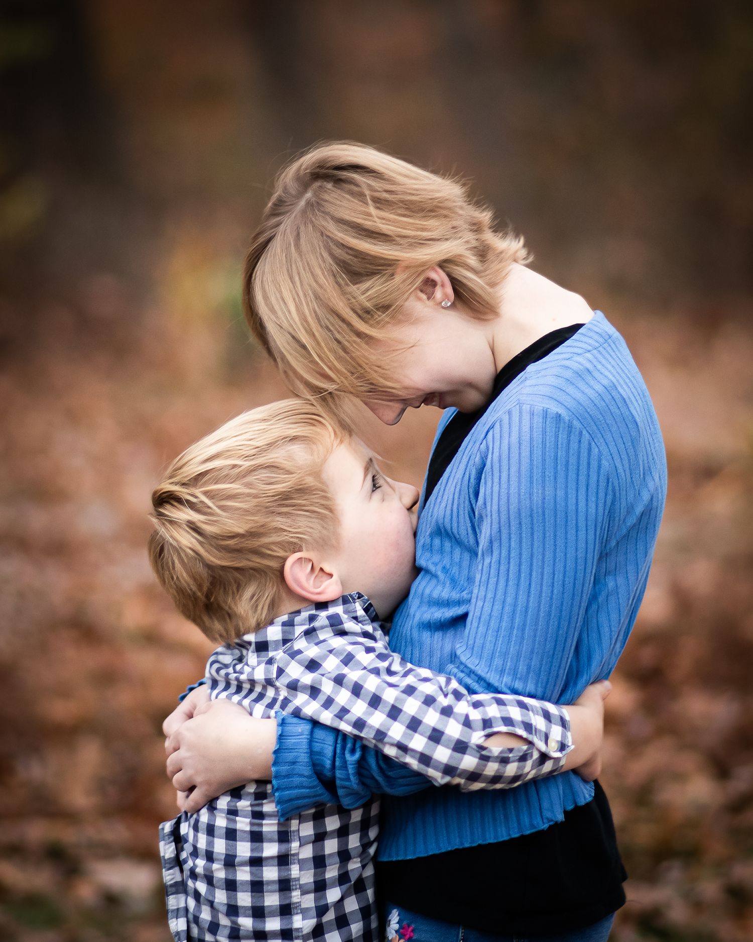 A woman and young boy share a warm embrace outdoors in an autumn setting, both wearing blue.