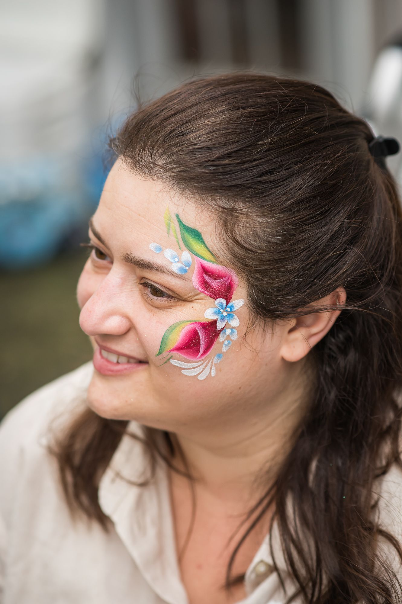 A smiling woman with floral face paint featuring pink flowers and blue accents on her cheek.