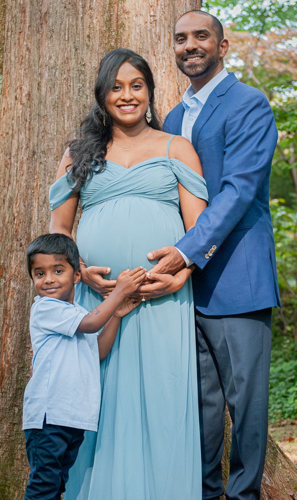 A family in coordinated blue outfits poses together against a rustic wooden backdrop during a maternity photoshoot.