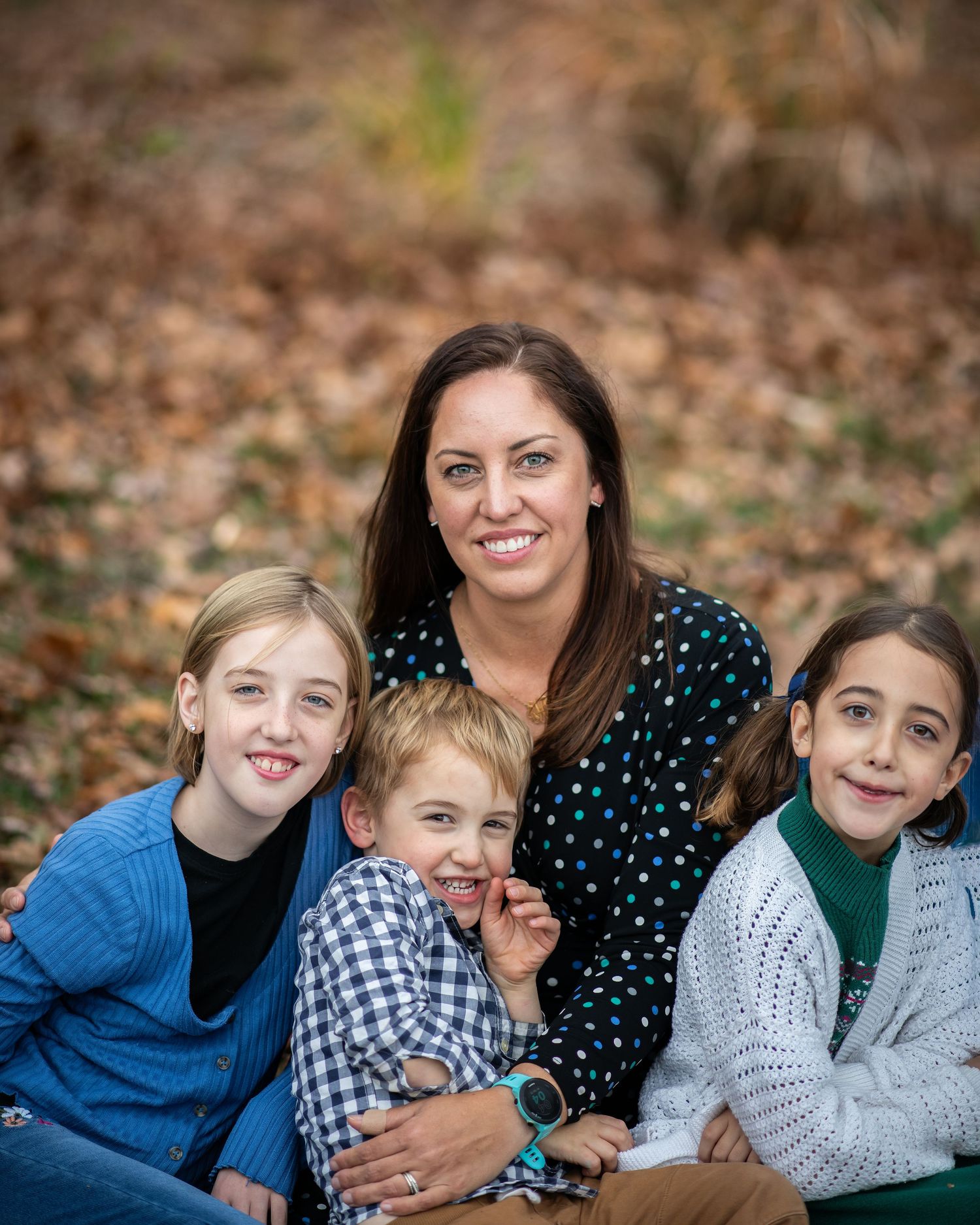 A group lounges together on fallen autumn leaves while smiling and laughing during an outdoor photo session.