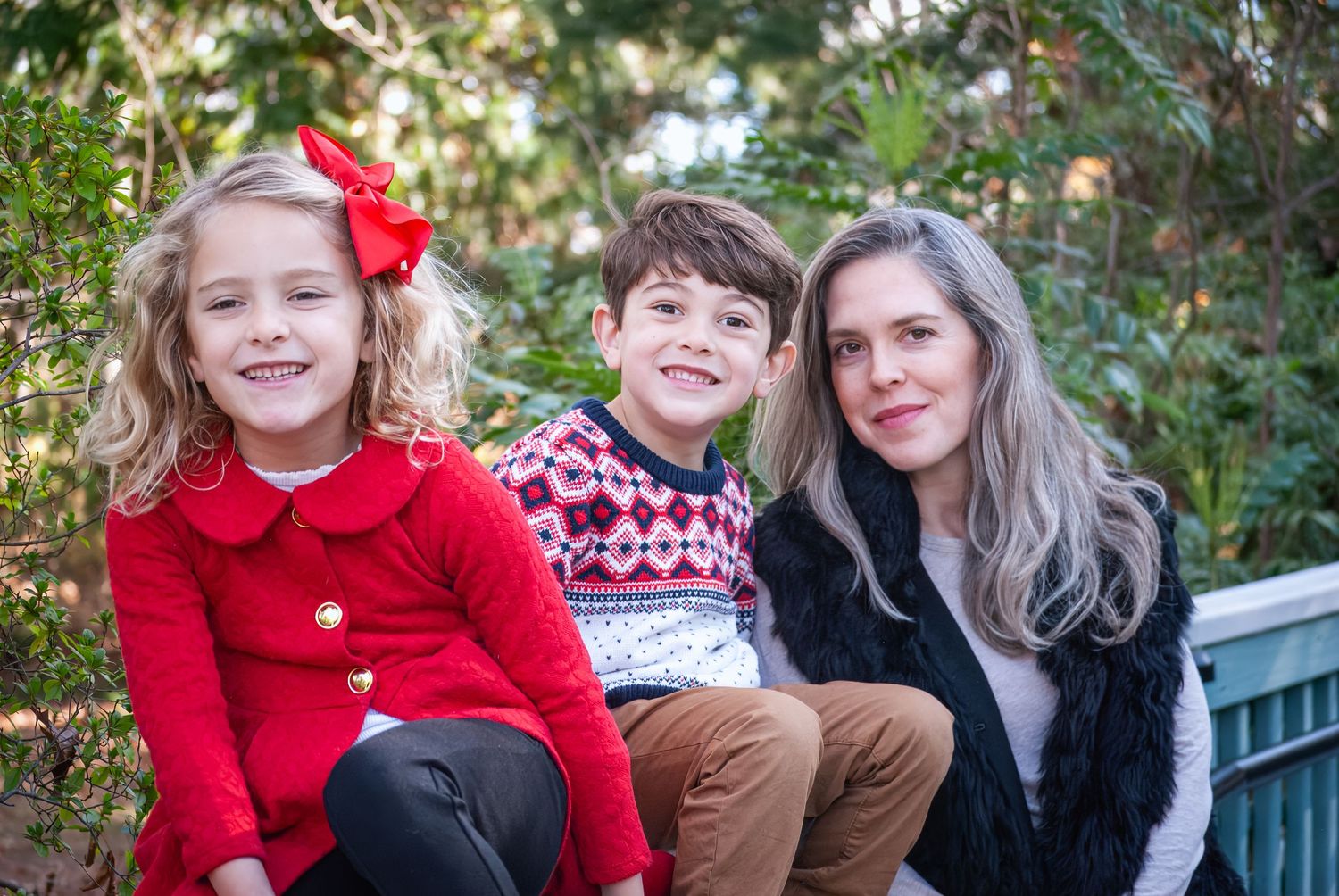 Family group wearing red and brown outfits poses together outdoors for holiday photos in natural setting.