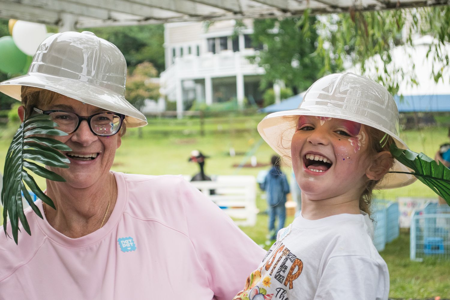 Woman and child laughing outdoors wearing white safari hats at a fun outdoor event on a green lawn.