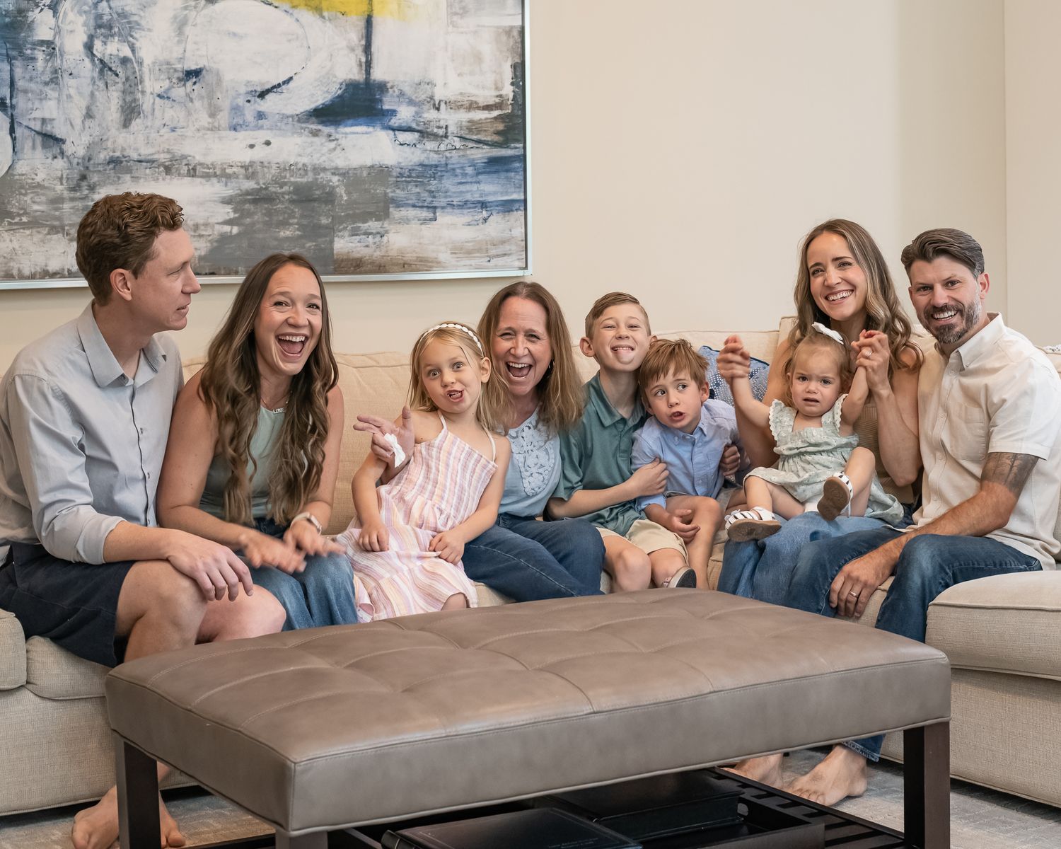 Happy family of adults and children smiling together on a couch in a bright, modern living room.