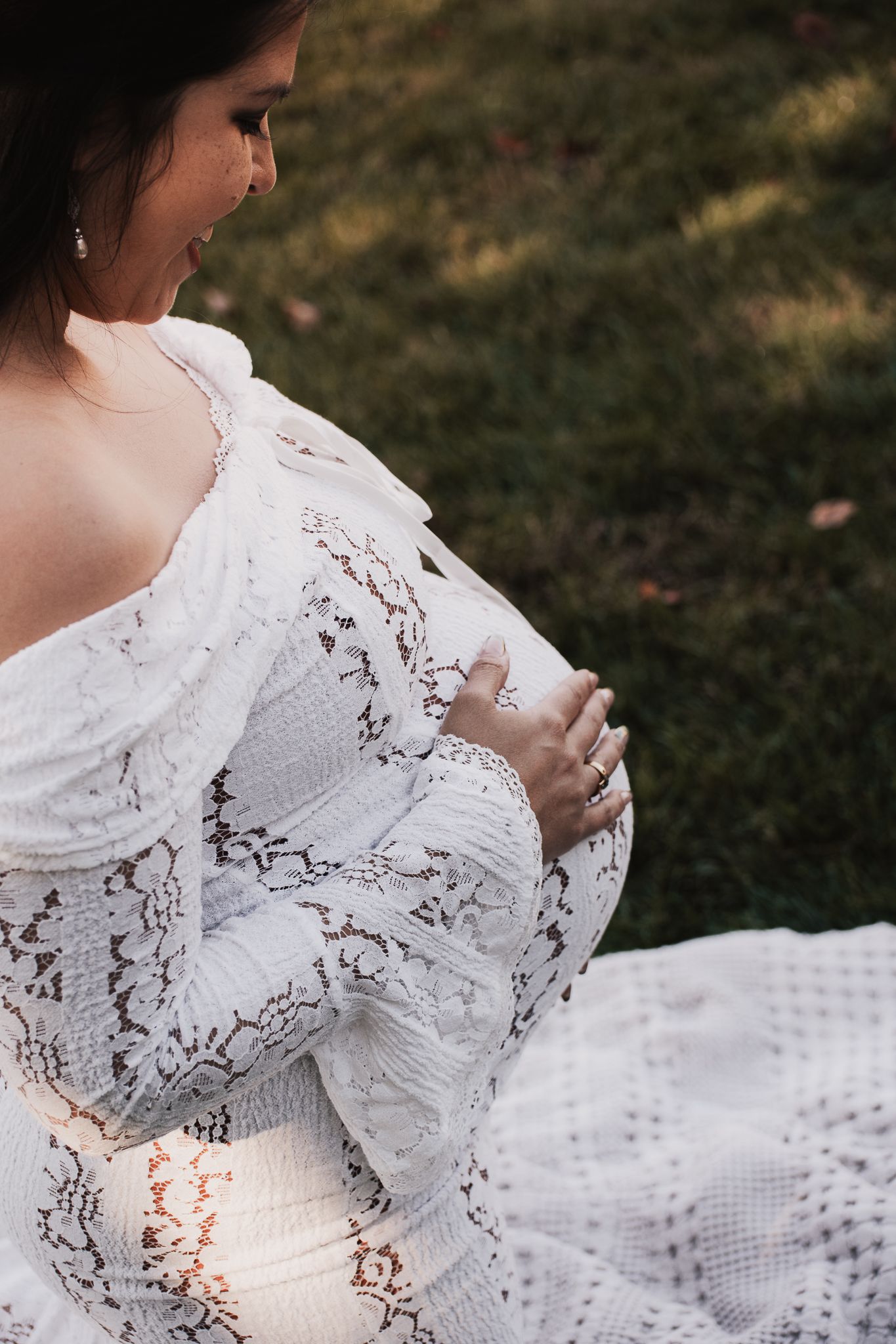 A woman in a white lace dress sits on grass while holding fairy lights creating a dreamy outdoor scene.