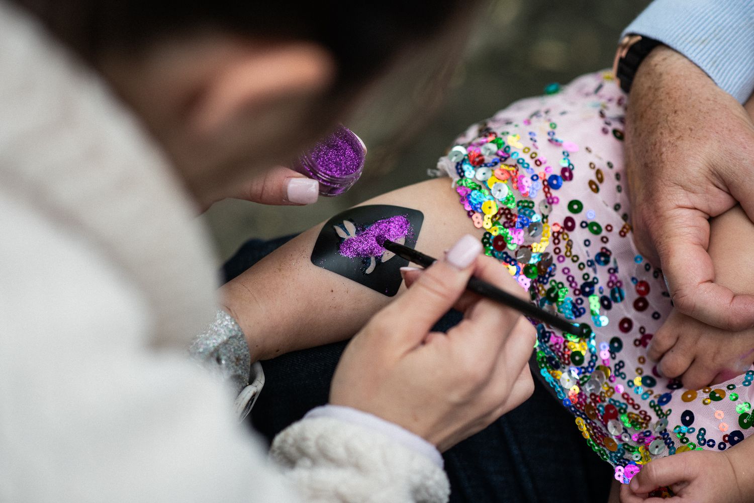 Artist applying a glittery purple unicorn temporary tattoo on a child's arm at a festive event.