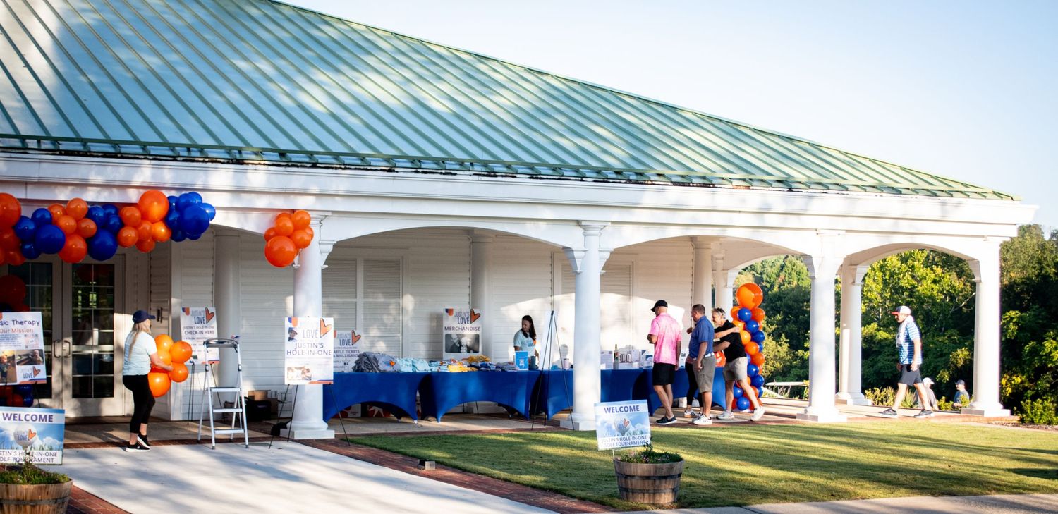 A series of white outdoor covered walkways with green roofs and orange decorations for an event or celebration.
