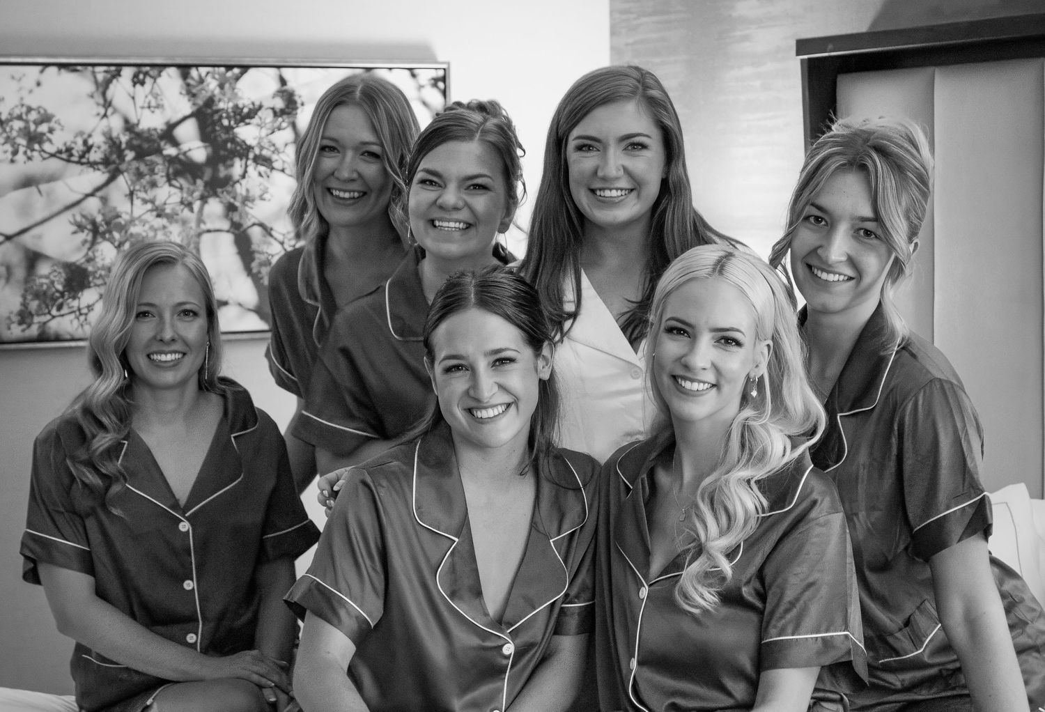 Black and white photo of a group of seven women smiling while wearing matching satin pajamas or robes.