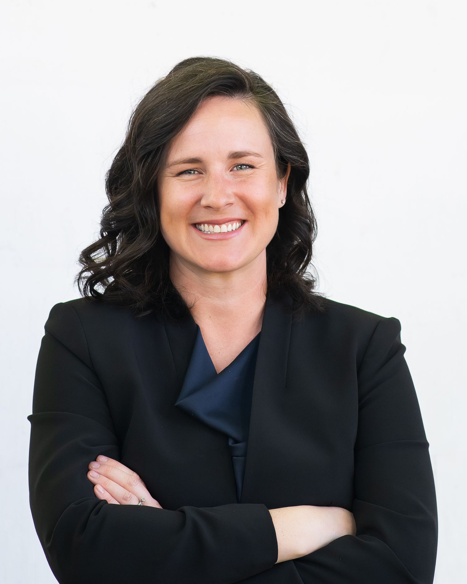 Professional woman in black blazer smiling with arms crossed against white background.