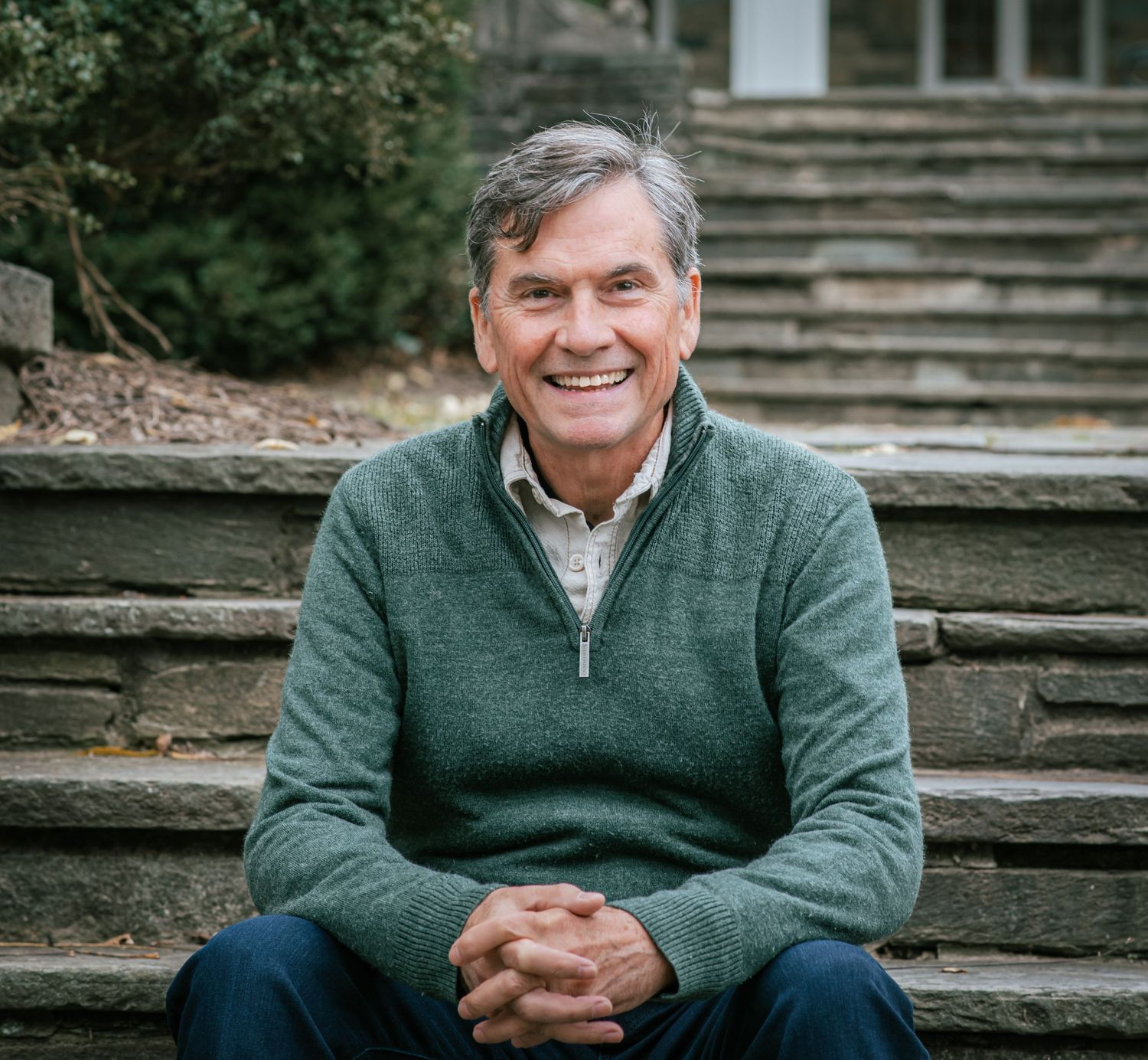 Person in green sweater sitting on stone steps outdoors smiling at camera in multiple similar poses.