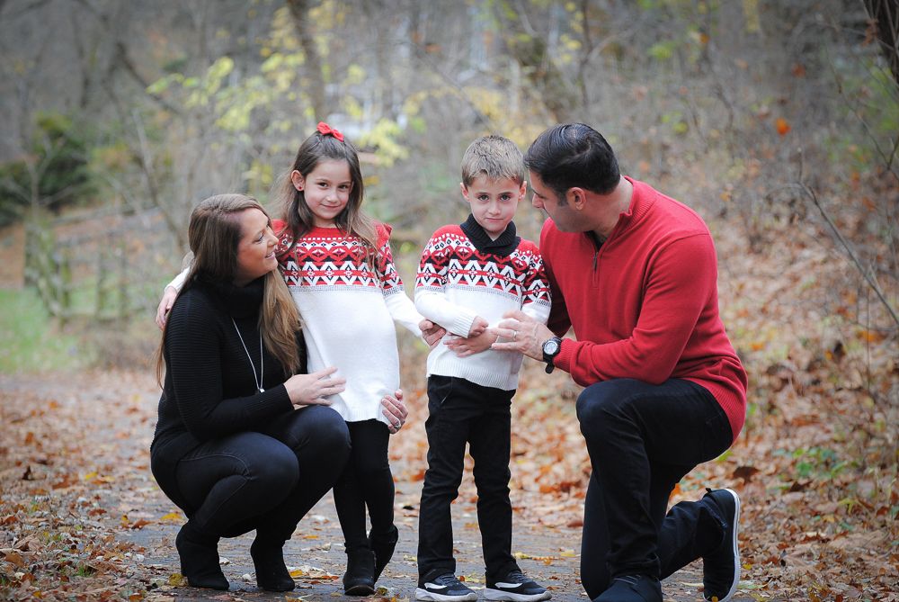 A family kneels together on fallen leaves examining something in the woods.
