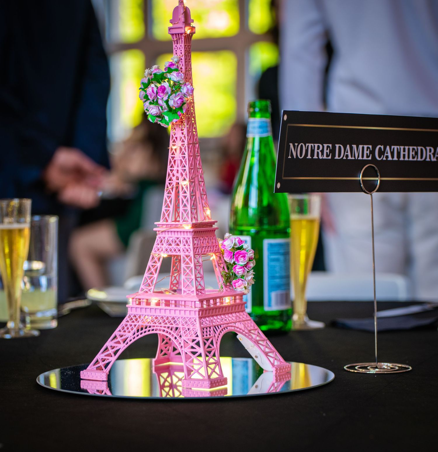 Pink miniature Eiffel Tower decorations displayed on tables at a themed event with ambient lighting and bottles in background.