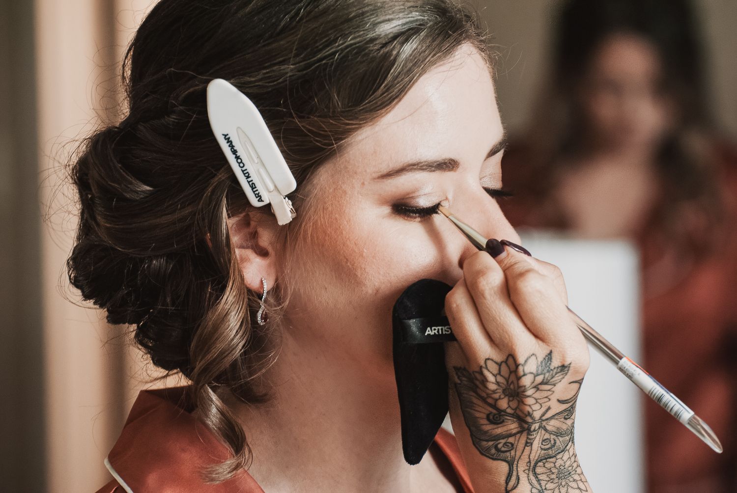 Makeup artist applying eyeliner to a bride with an updo hairstyle on her wedding day.