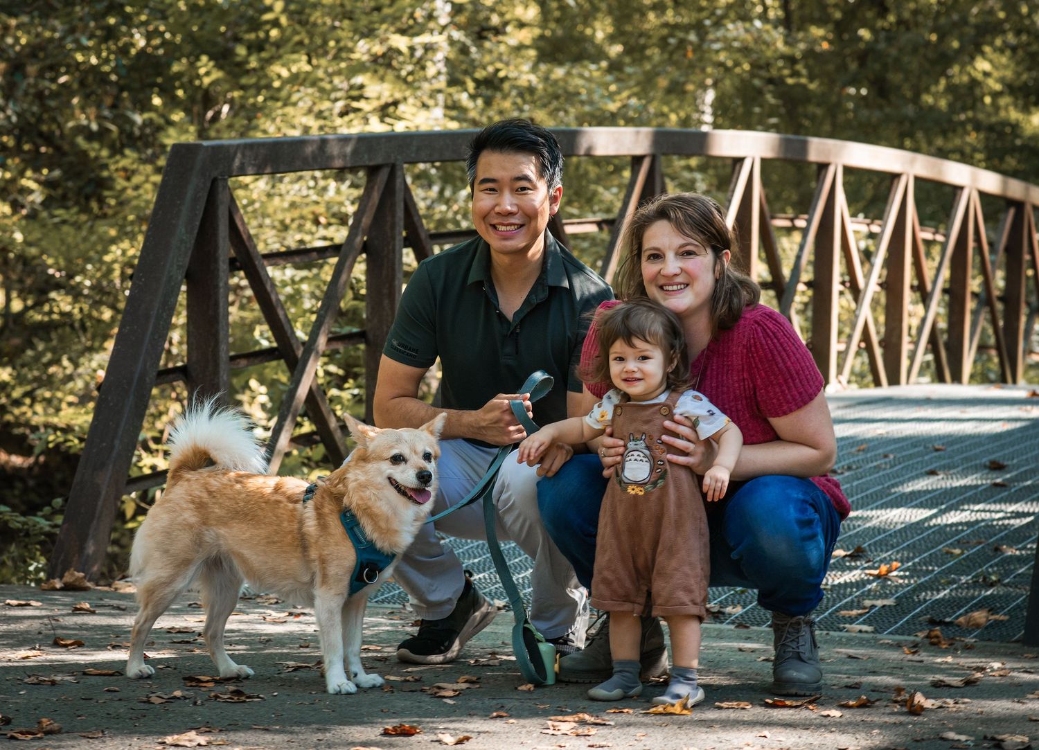 Family sitting together on a wooden bridge in a park during a sunny autumn day.
