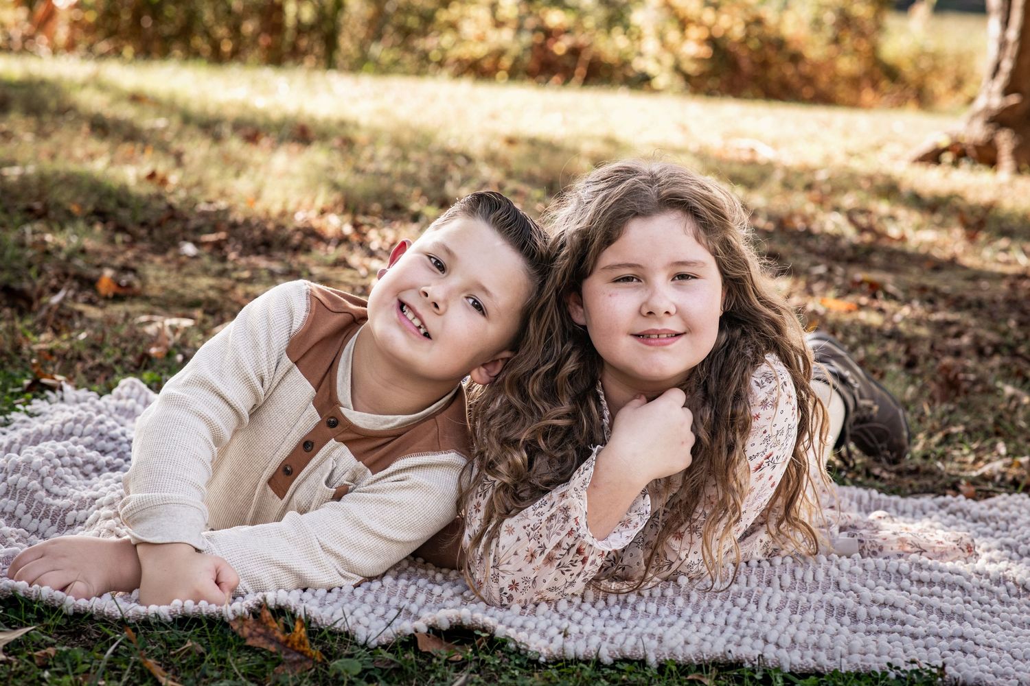 Two children laying on a blanket outdoors in autumn laughing and playing together in natural sunlight.