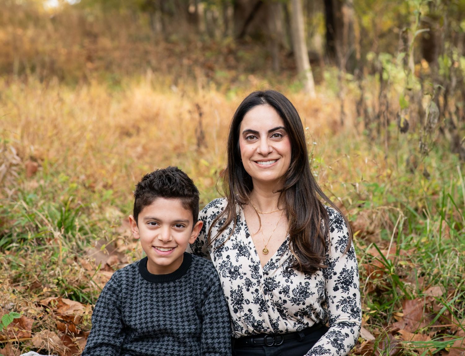 A family sits together outdoors during autumn with fallen leaves and natural lighting in the background.