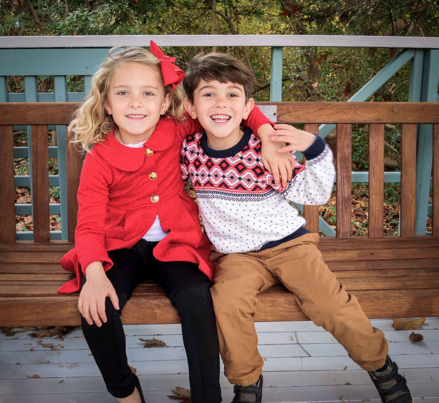 Four candid photos on a wooden bench show children in red sweaters and brown pants enjoying a playful moment together.