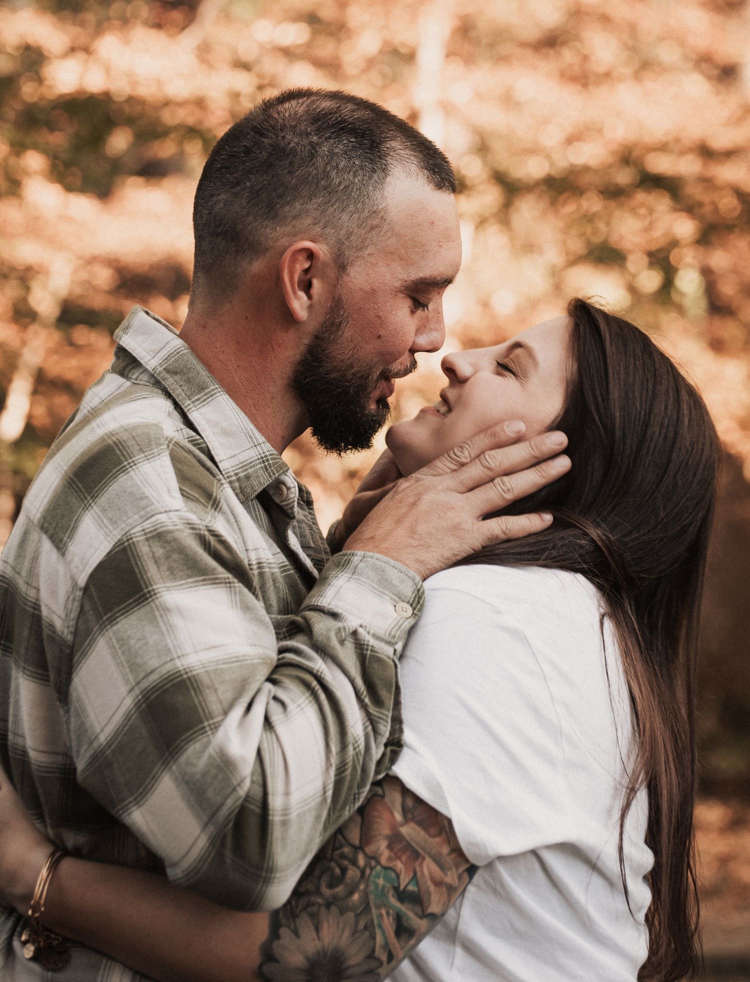 A couple shares a romantic almost-kiss outdoors in autumn, the man cradling the woman's face tenderly.