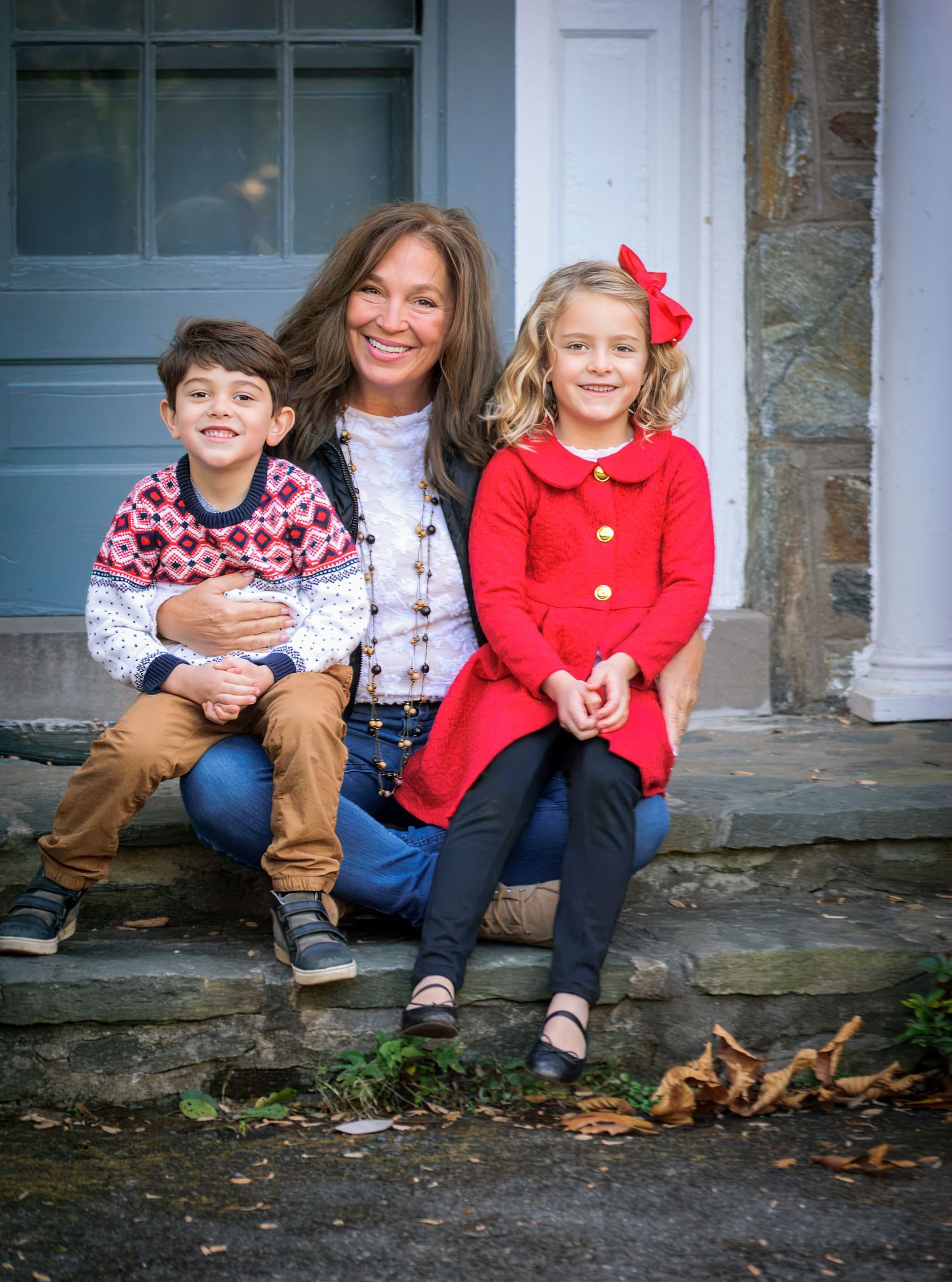 Family sitting on stone steps in front of blue door during autumn photoshoot.