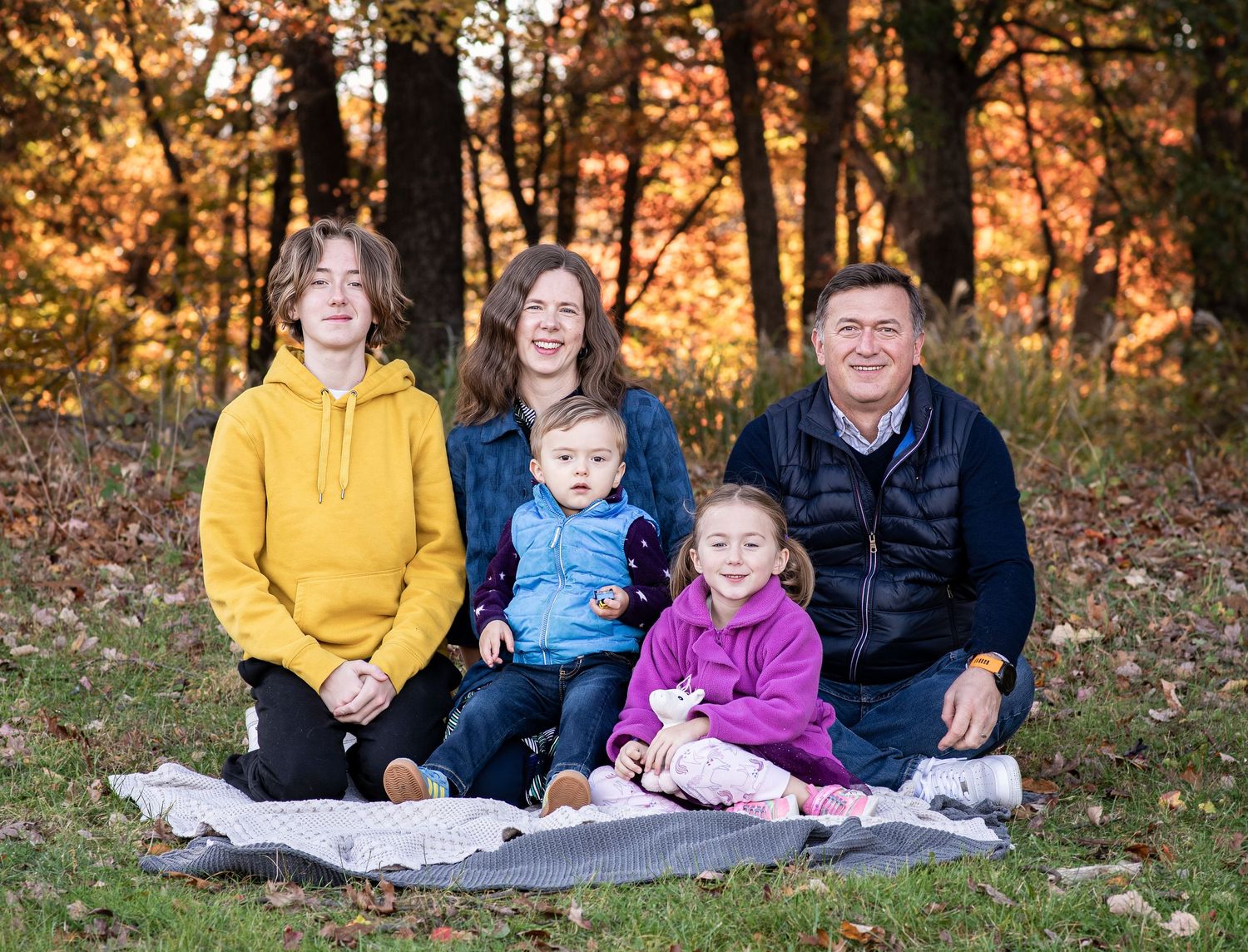 A group sits together on a blanket in an autumn forest setting during golden hour.