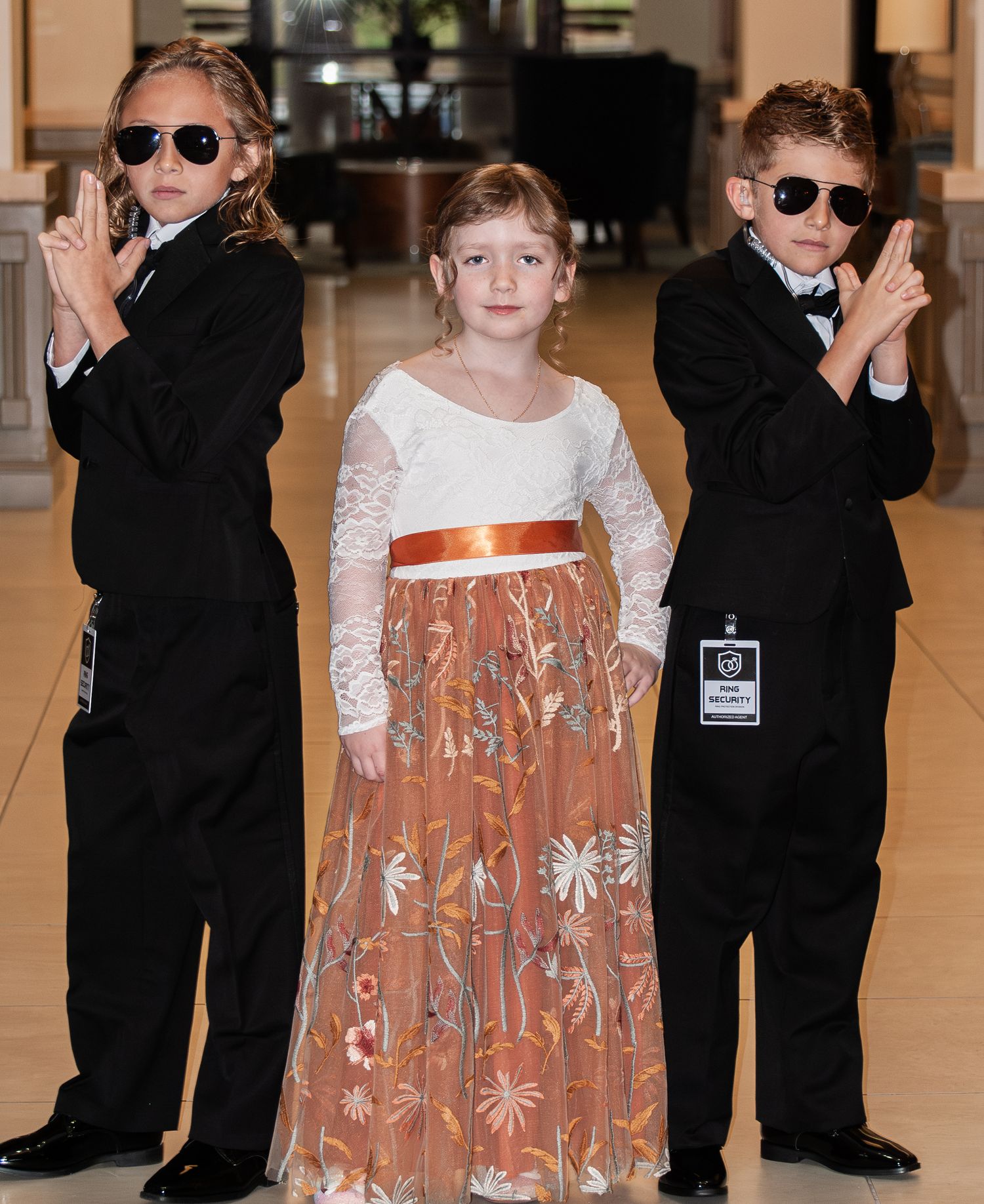 Two people walking through a hallway, one wearing sunglasses and black clothing, the other in a white and orange dress.