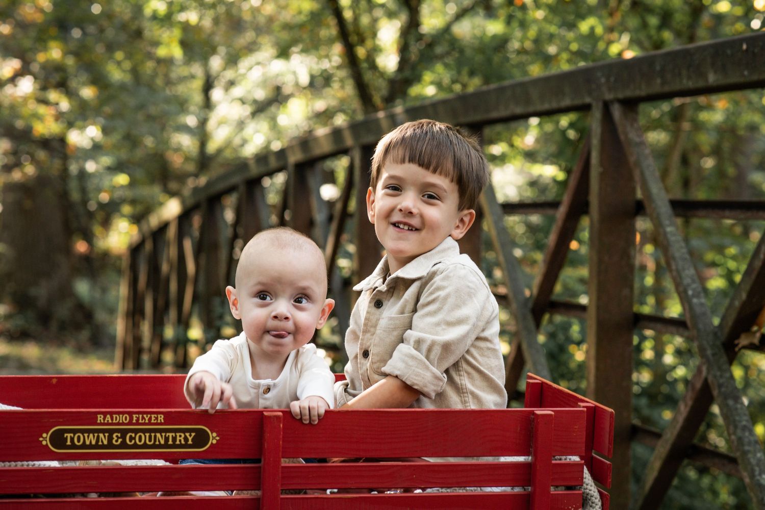 Children sit and play together in a red wagon on a sunny autumn day in the park.