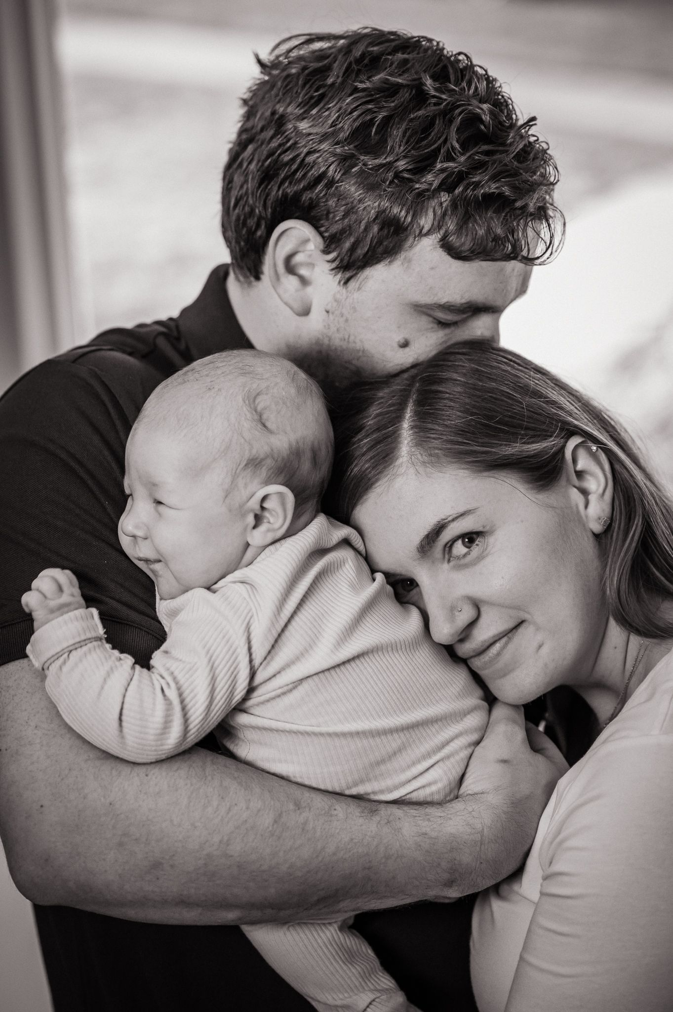 Black and white photos capturing tender family moments as parents cuddle their newborn baby.