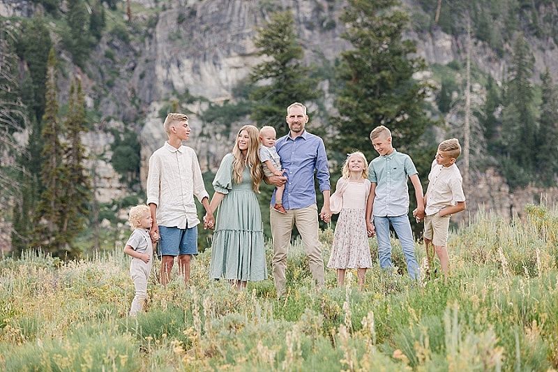 A group stands together in a scenic mountain meadow wearing coordinated pastel outfits for a summer photo session.