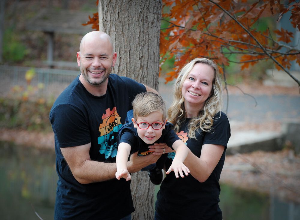 A family poses playfully together against a tree during autumn by a lake.
